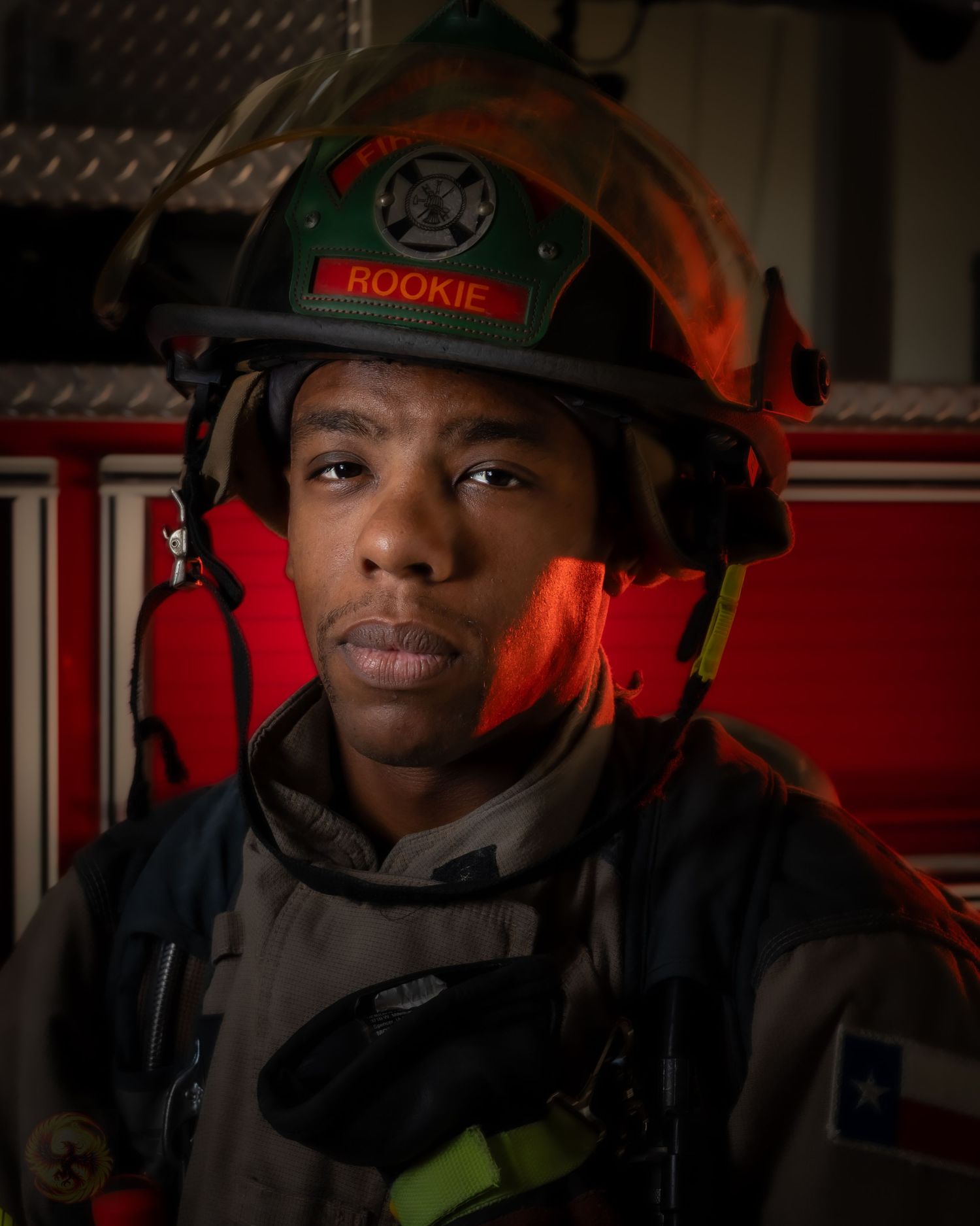Firefighter rookie in protective gear and helmet illuminated by dramatic red lighting.