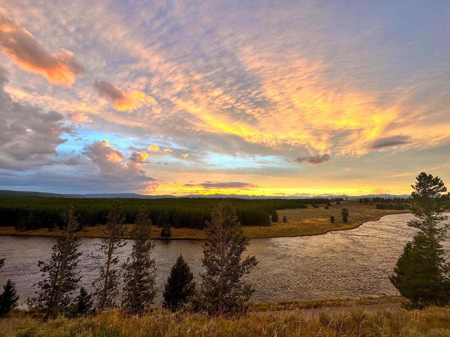 Stunning panoramic sunset with orange and purple clouds stretching across mountain landscape.