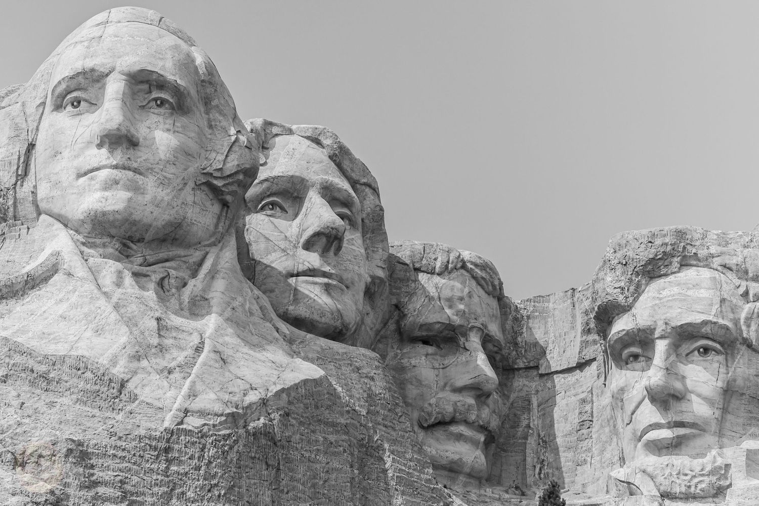 Black and white photograph of Mount Rushmore showing the carved presidential faces against a cloudy sky.