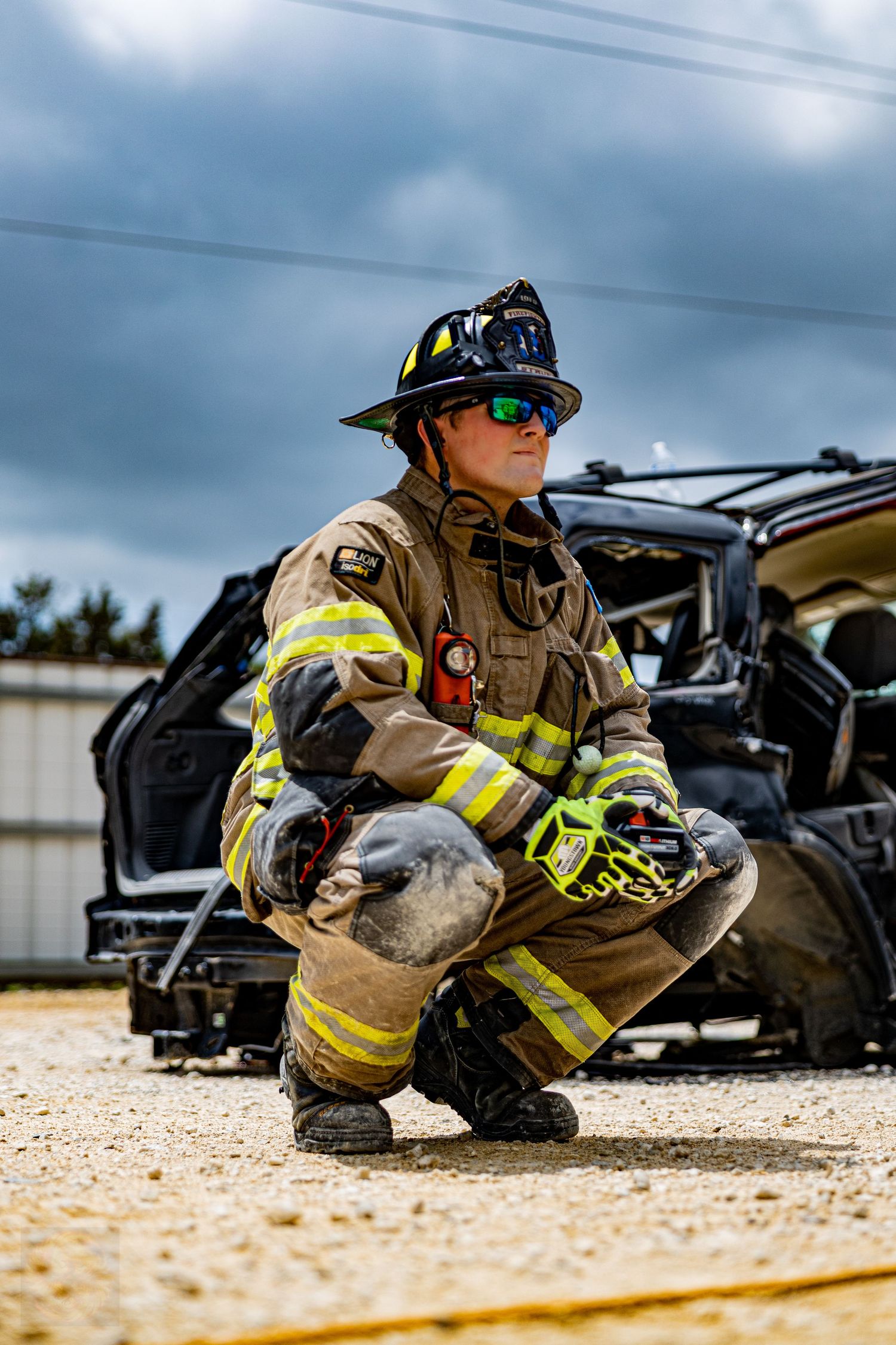 Firefighters in protective gear crouch near emergency vehicles during a training exercise.