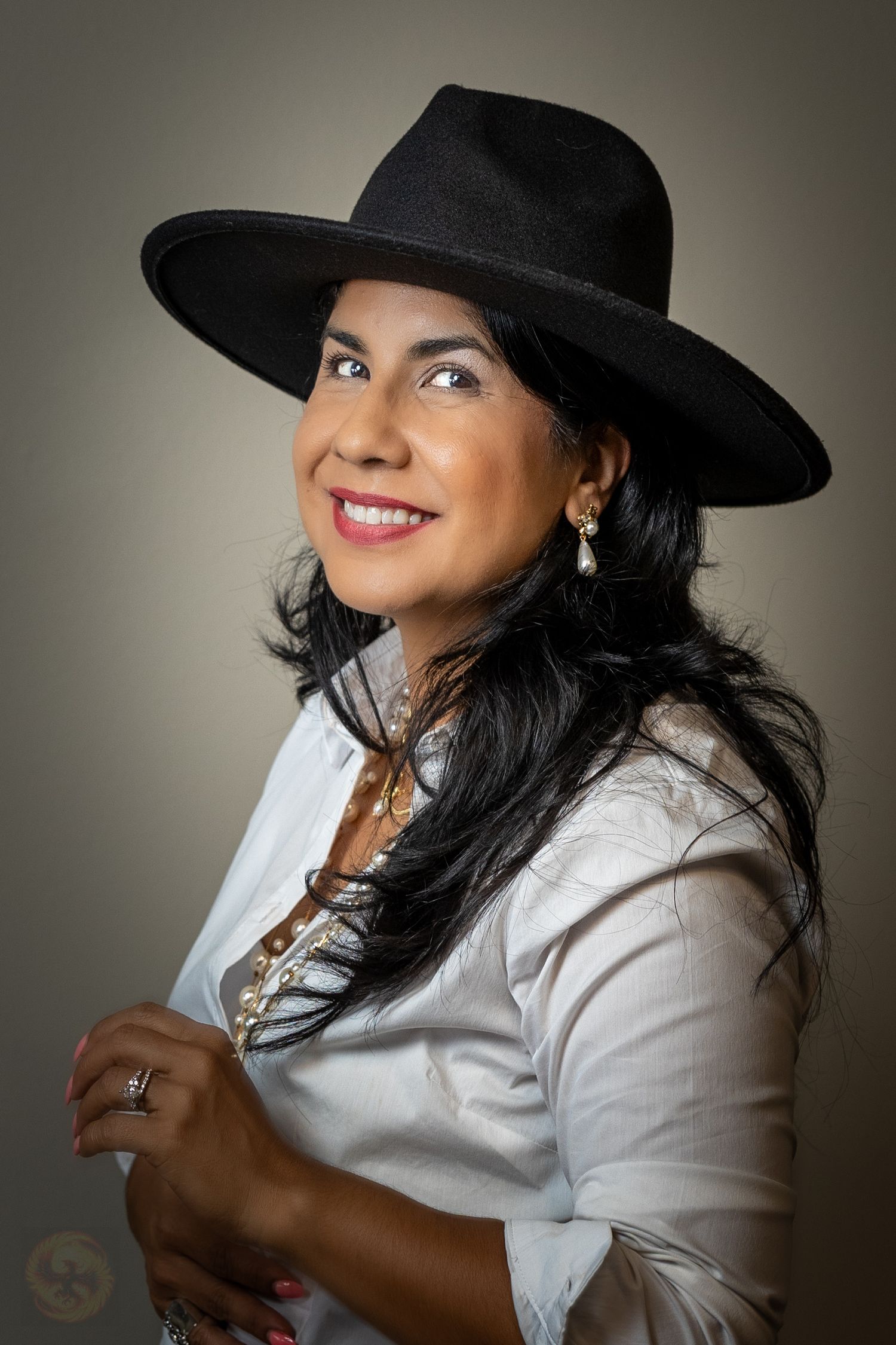 Studio portrait of a person wearing a black wide-brimmed hat and white blouse.