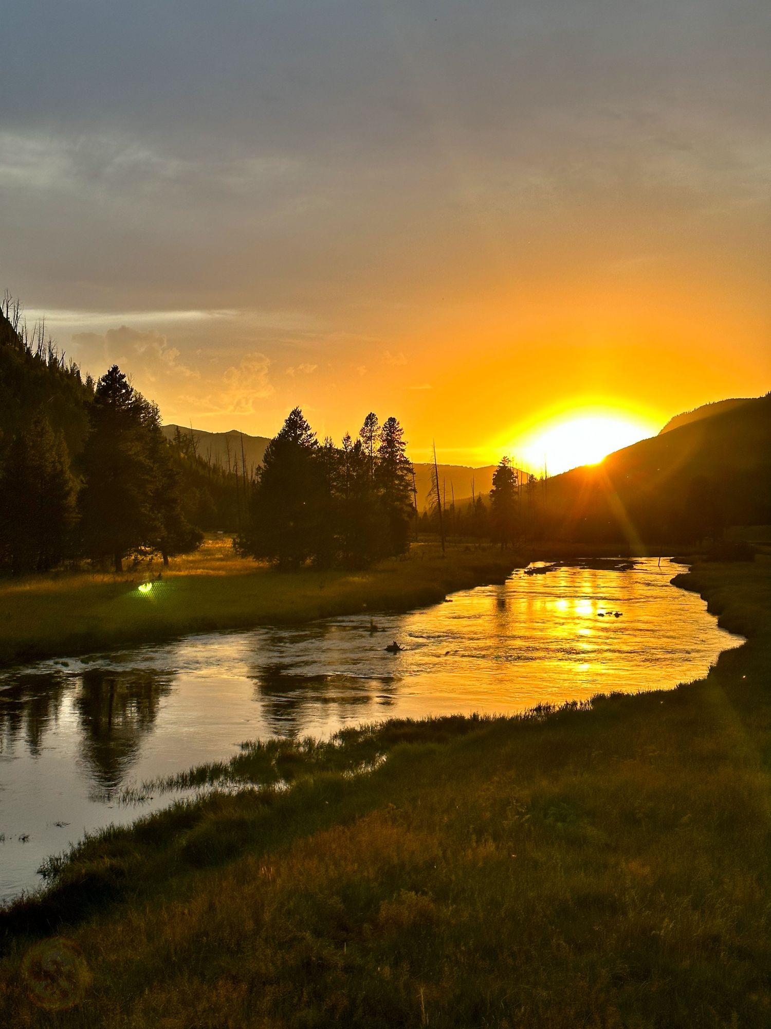 Stunning sunset over a river valley with mountains silhouetted against an orange sky.