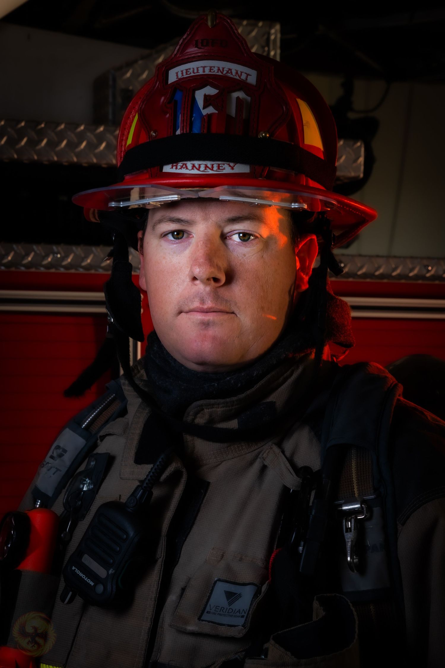 Firefighter in full protective gear and red helmet in dramatic lighting.