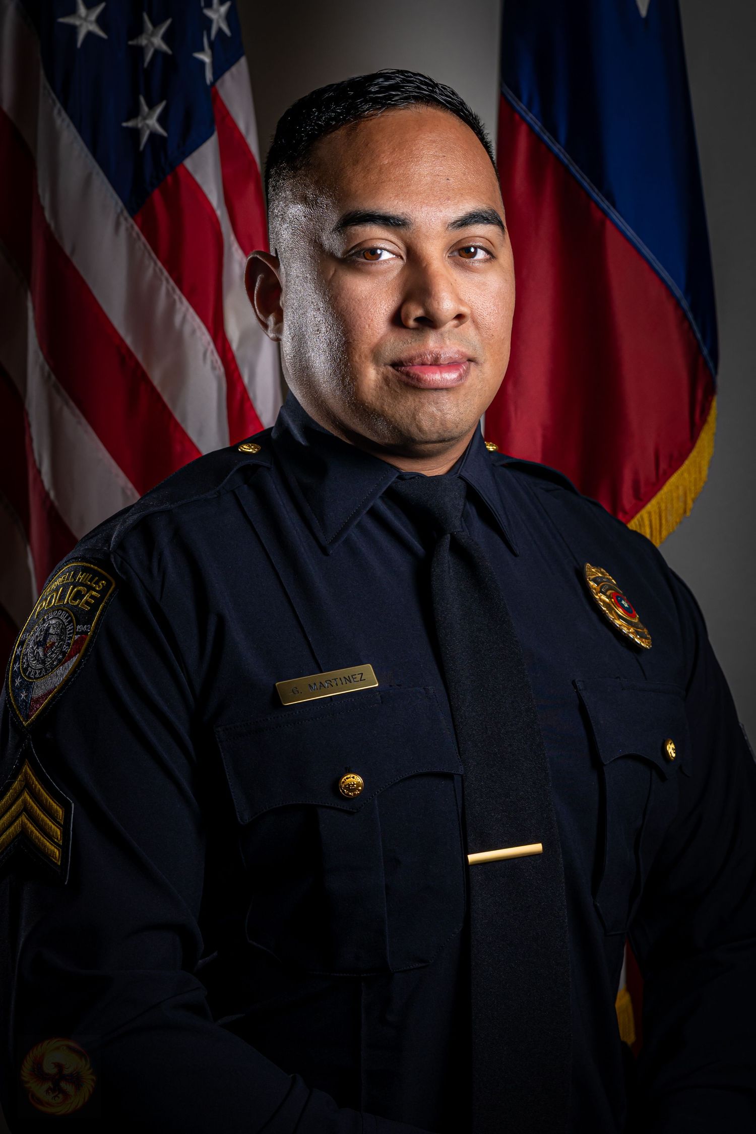 A police officer poses for official portraits in front of American flags.