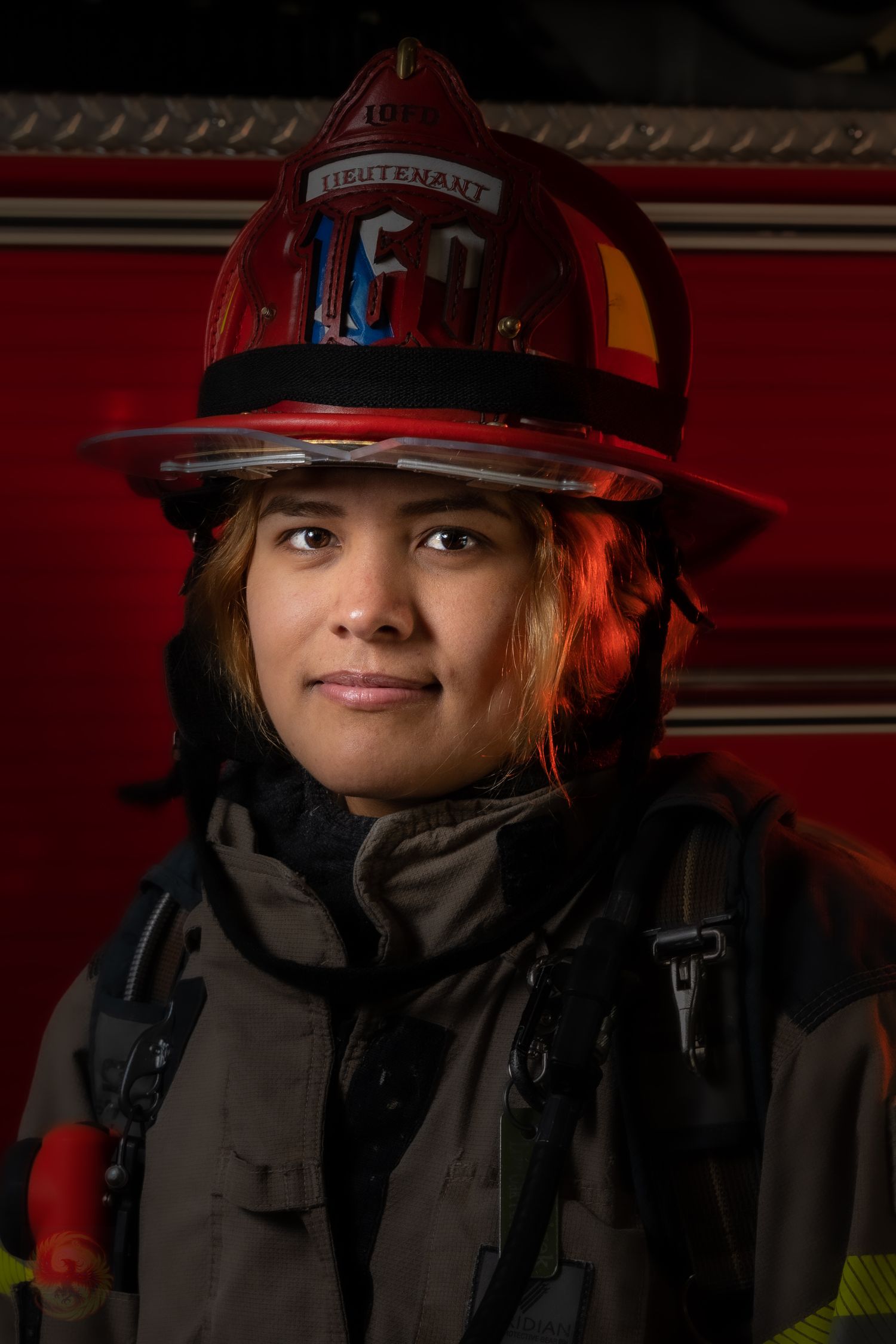 Firefighter in protective gear and red helmet against dark red background.