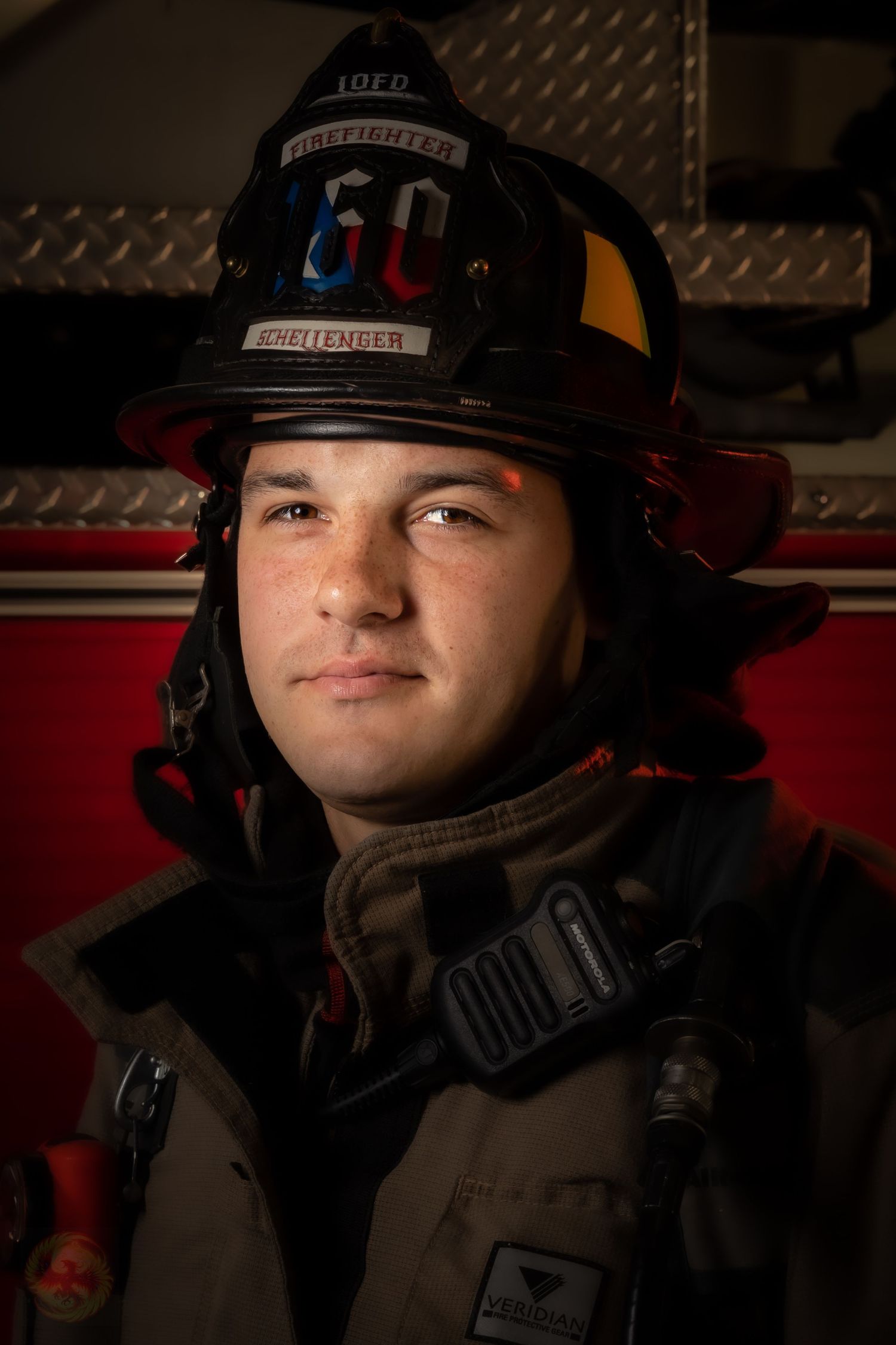Portrait of a firefighter wearing protective gear and helmet in front of a fire truck.