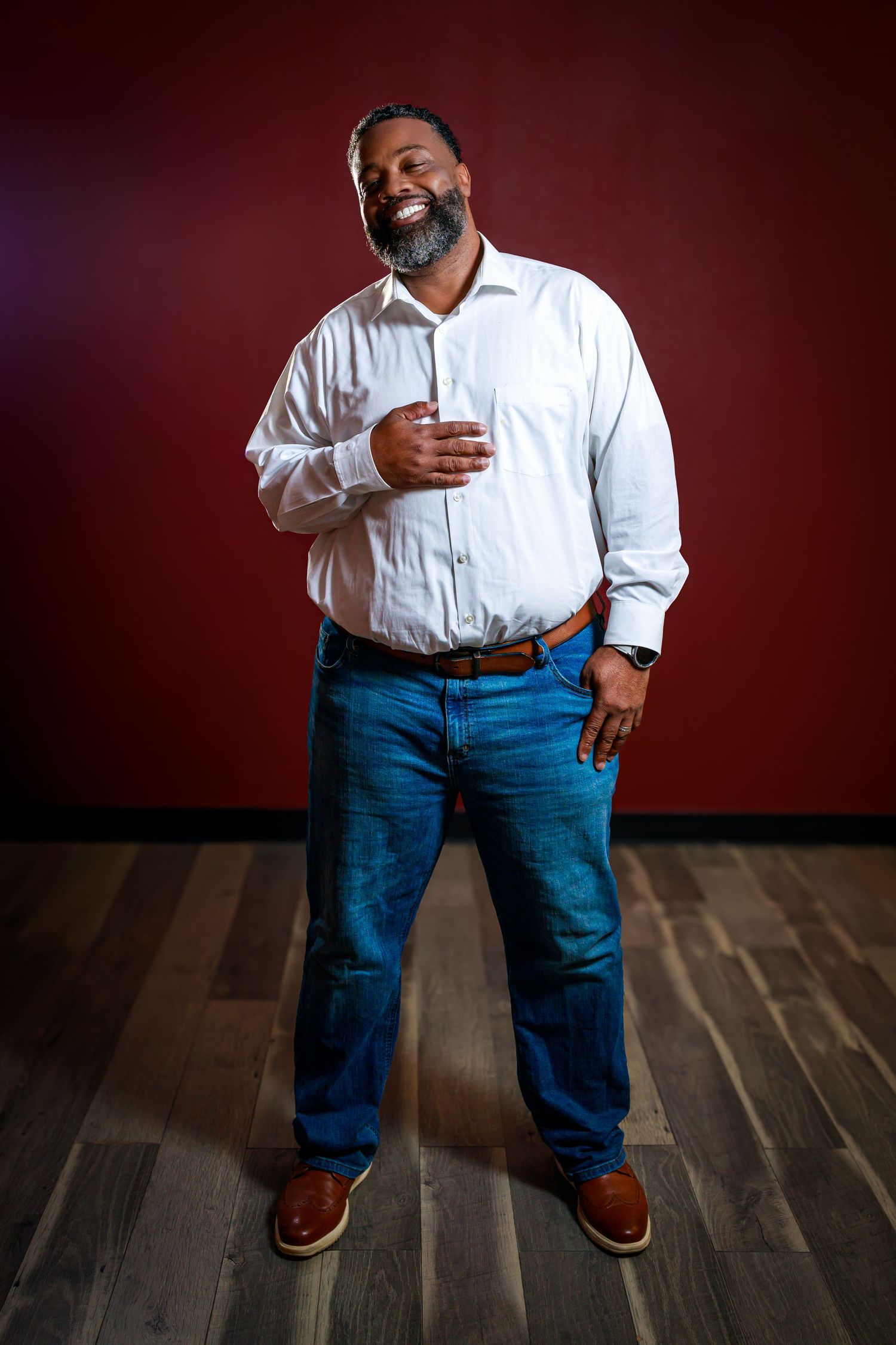 Person in white shirt and blue jeans stands against red wall in artistic portrait series showing different poses.