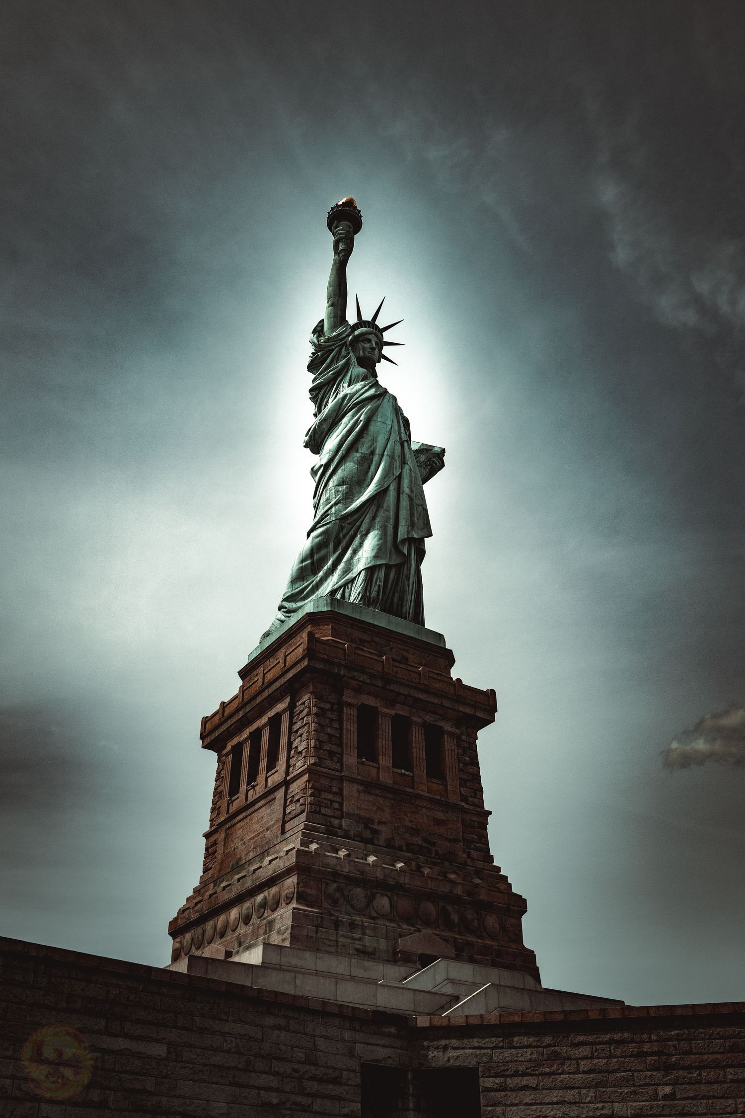 Statue of Liberty photographed from below against moody cloudy sky.