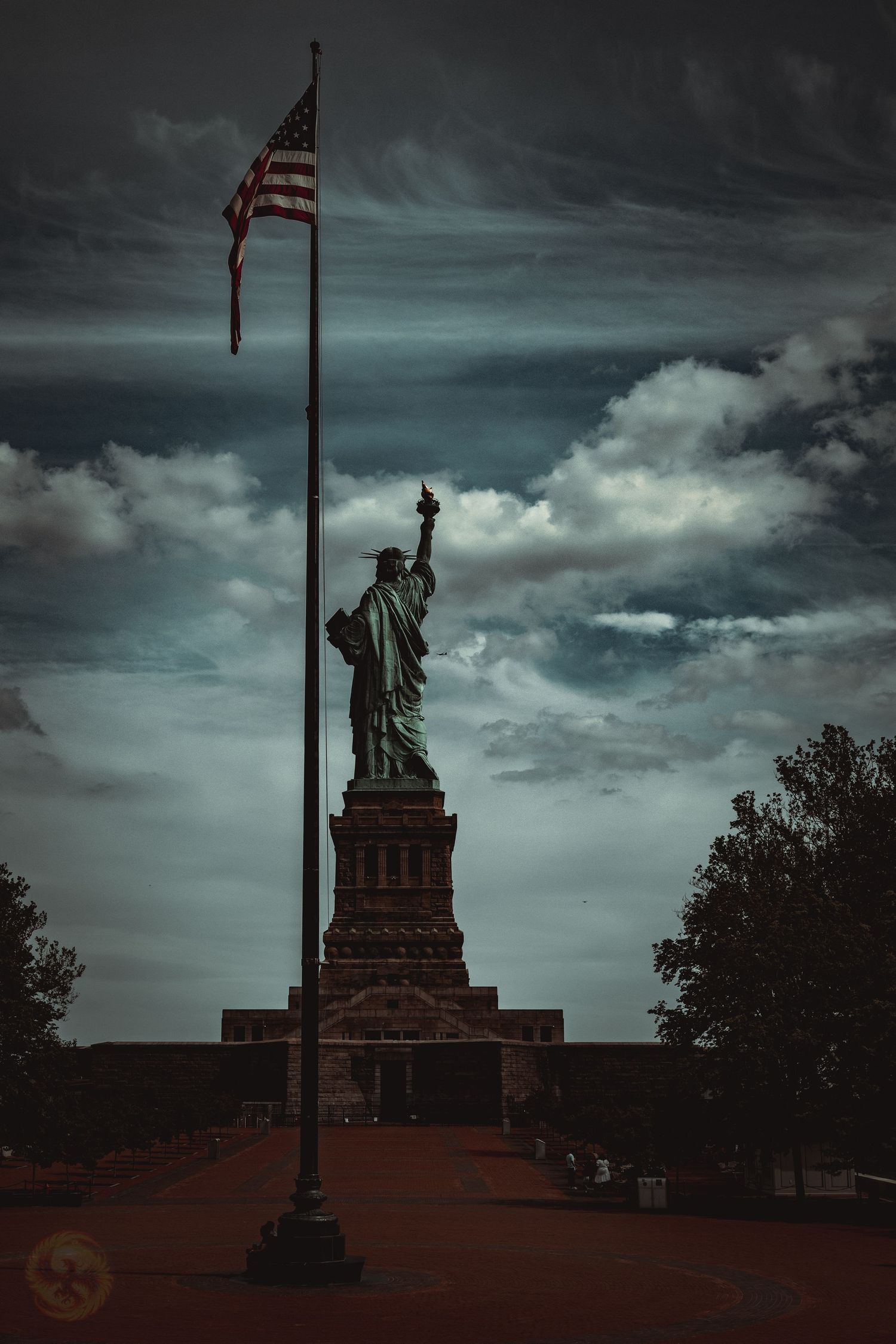 Statue of Liberty silhouette against dramatic stormy sky with American flags.