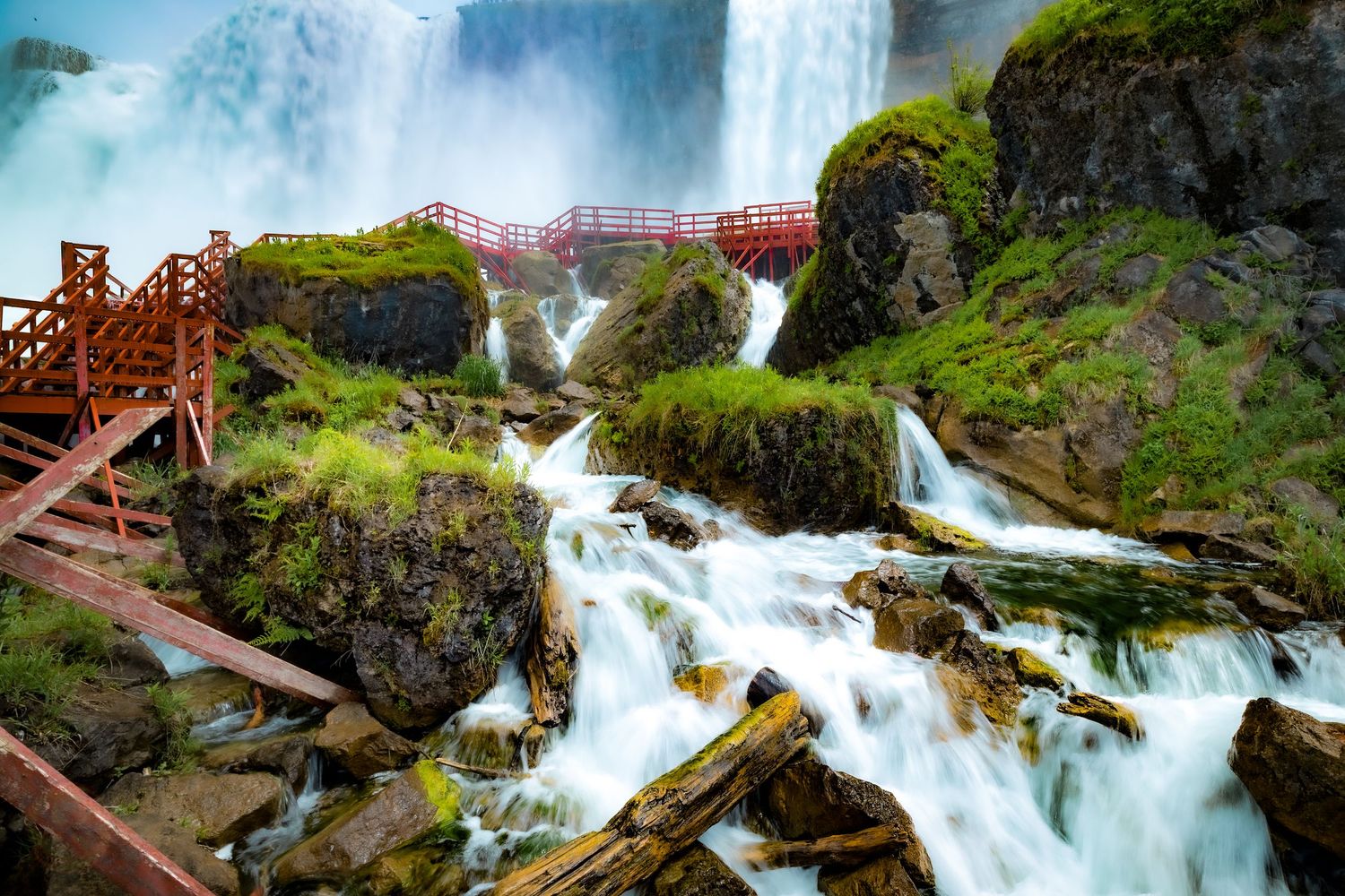 Dramatic waterfall cascades over rocks with red wooden walkways crossing above.