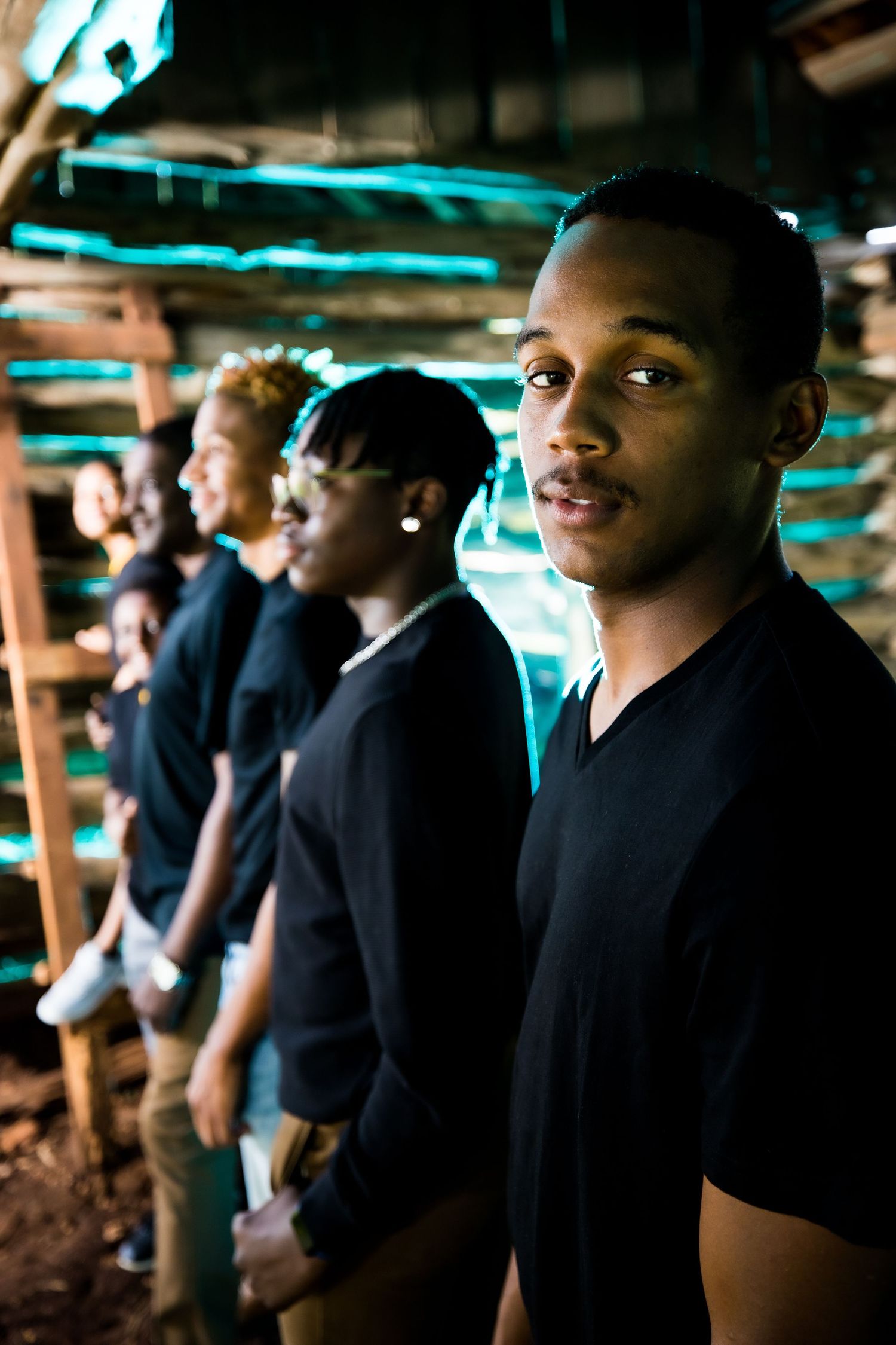 A group of people wearing black shirts stand in line under turquoise lighting in a dark space.
