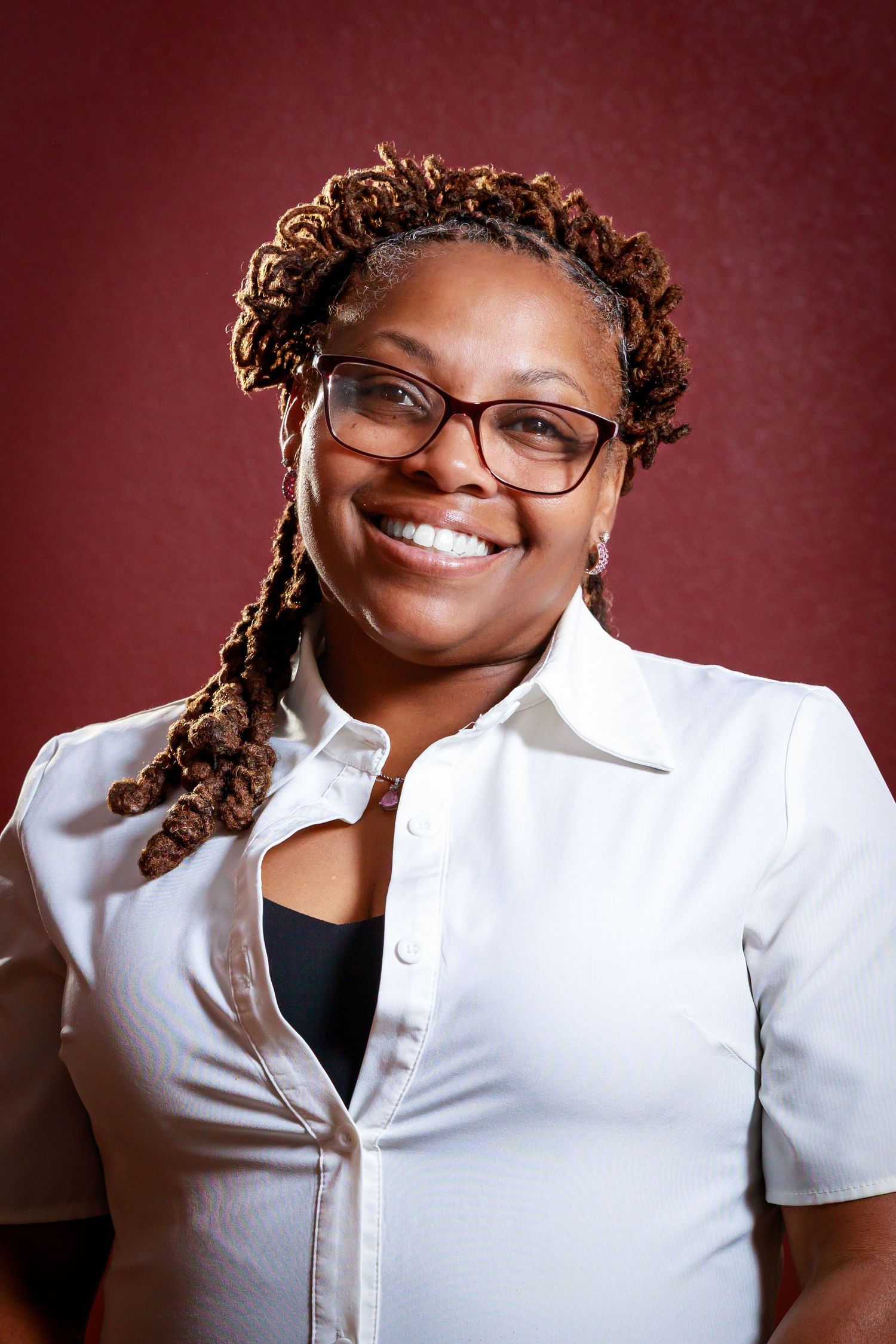 Professional headshot portraits against burgundy background showing warm expressions and white collared shirt.