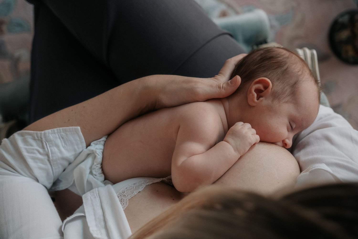 Newborn baby in diaper sleeping peacefully while breastfeeding on mother's lap.