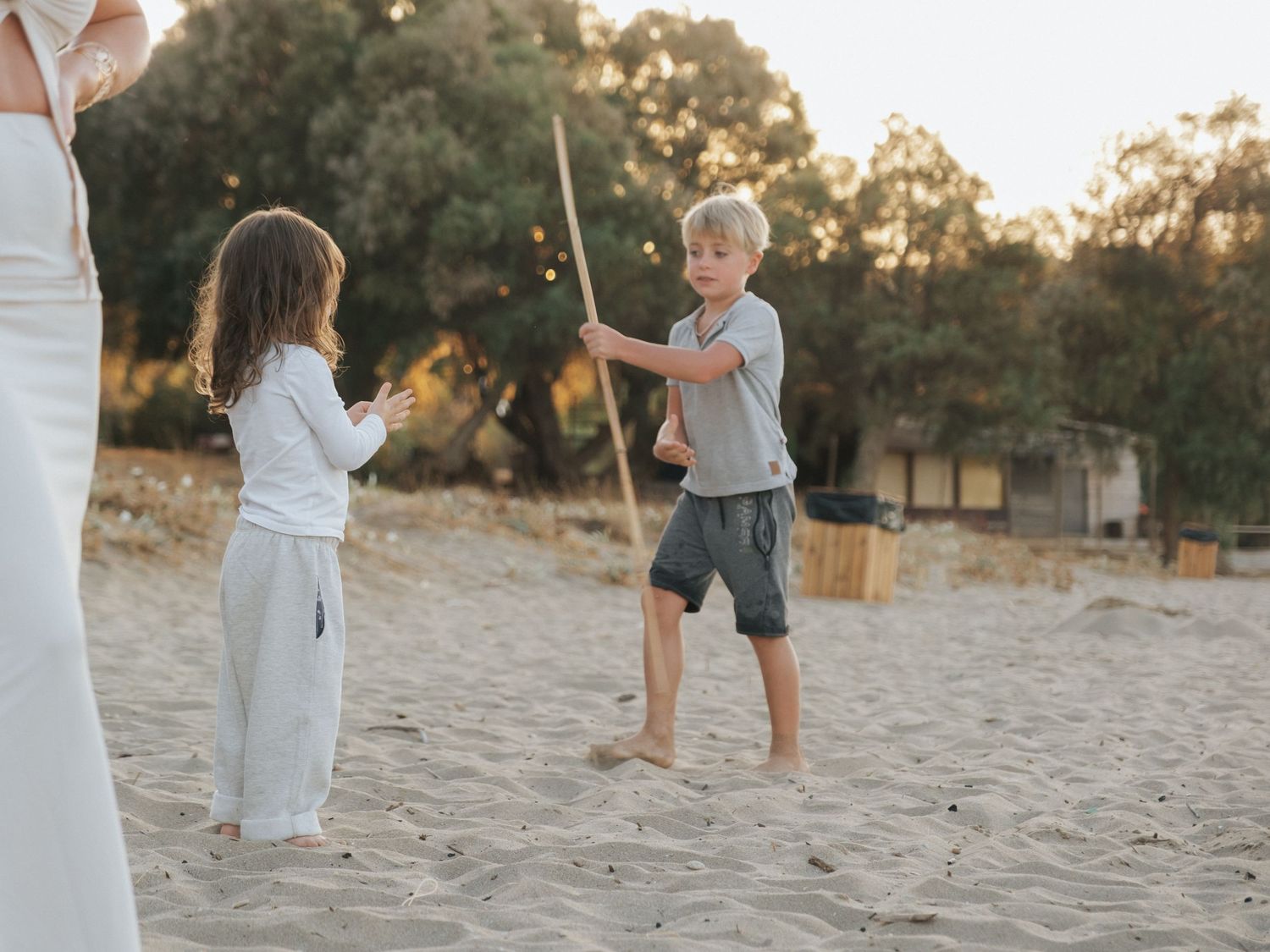 Two young children playing with a stick in the sand at sunset.