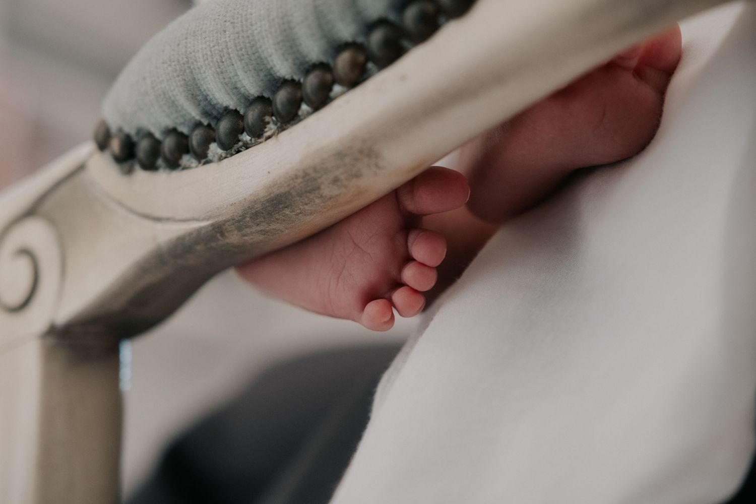 Tiny newborn baby feet resting on a white wooden chair with beaded decor detail.