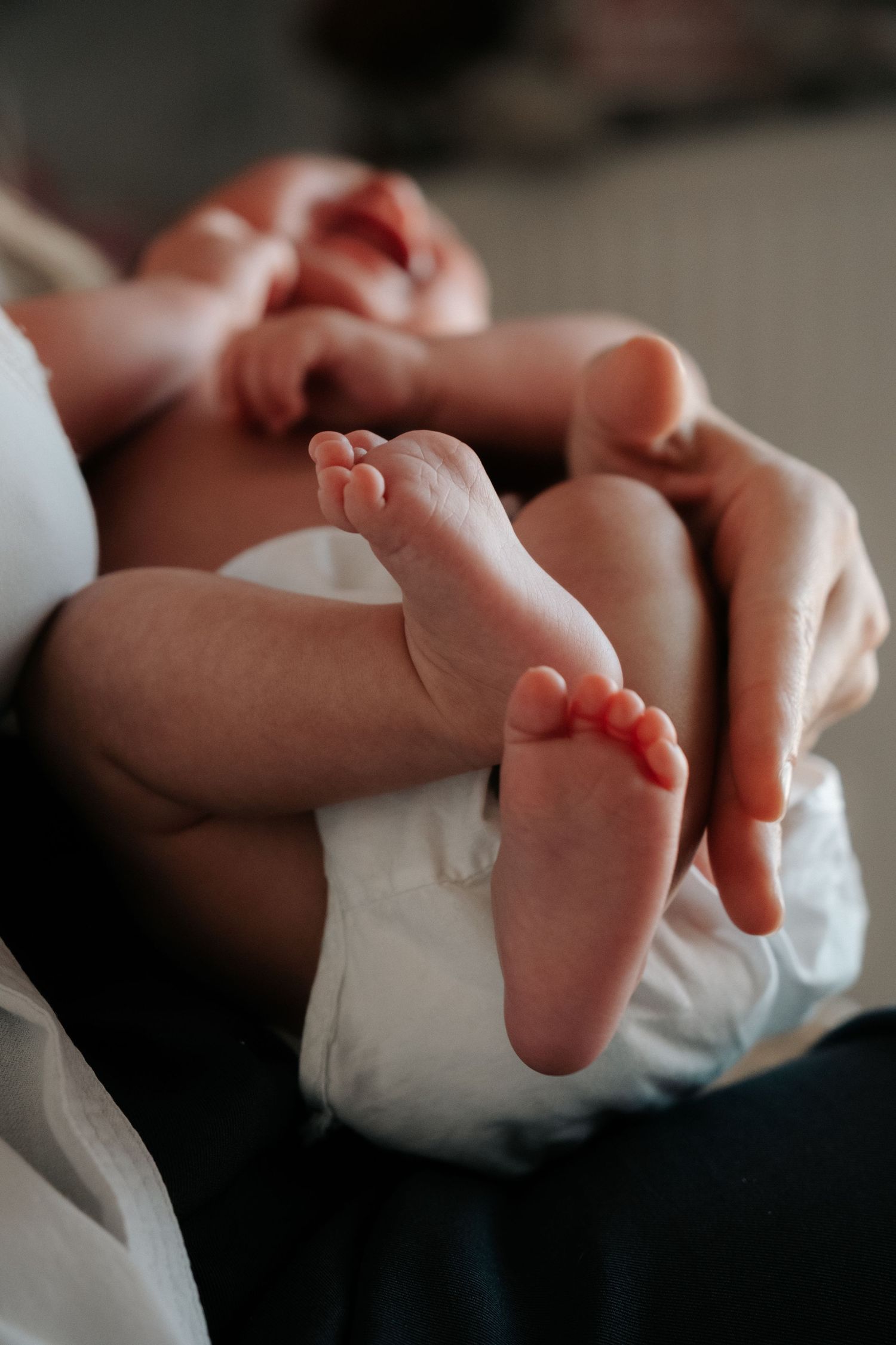 Parent cradling a newborn baby, showcasing the infant's tiny feet and toes in a tender moment.