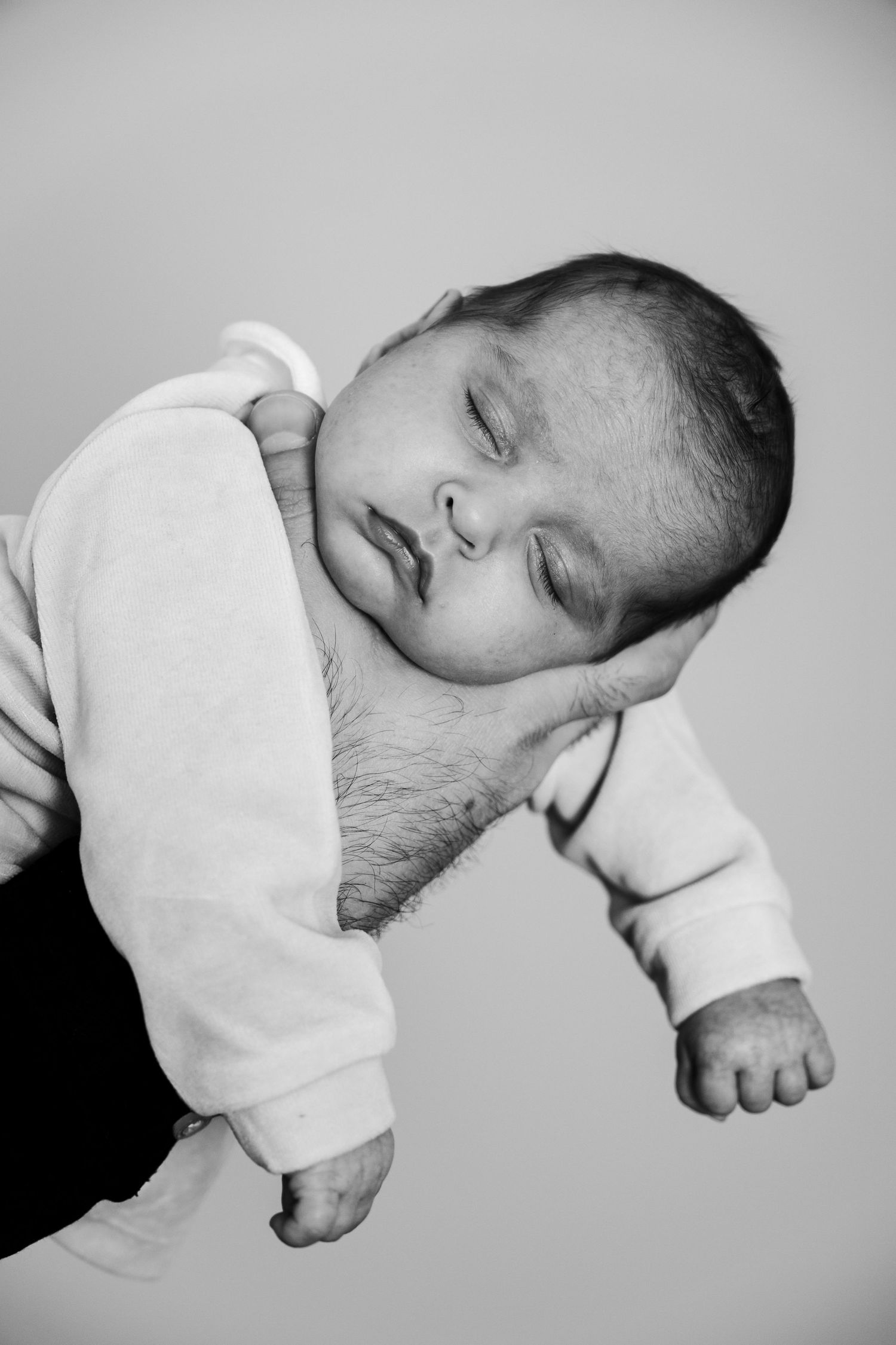 Black and white portrait of a sleeping newborn baby cradled gently in a parent's arms.