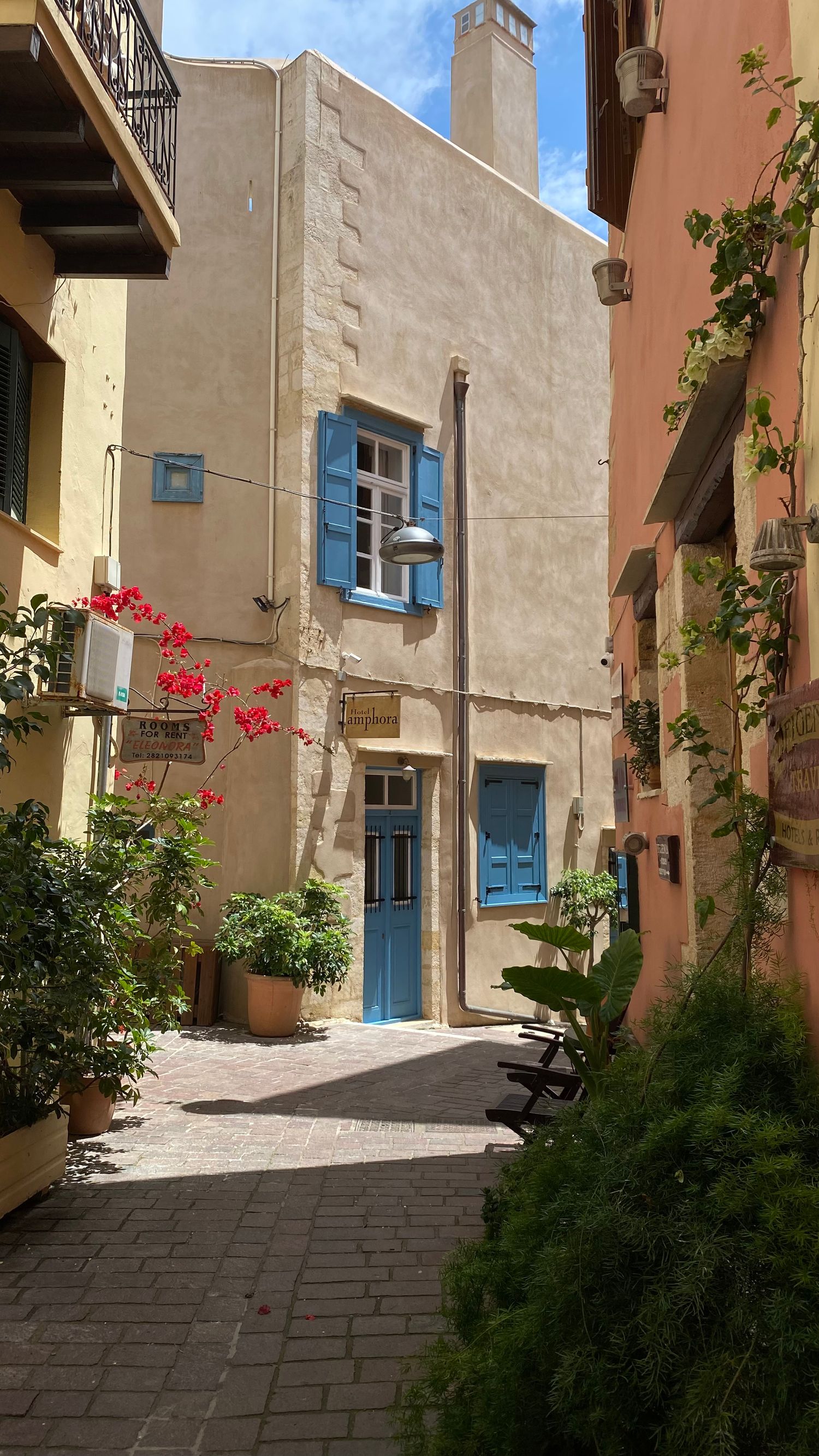 Quaint Mediterranean courtyard with blue shuttered windows and doors on cream stone building with climbing plants.