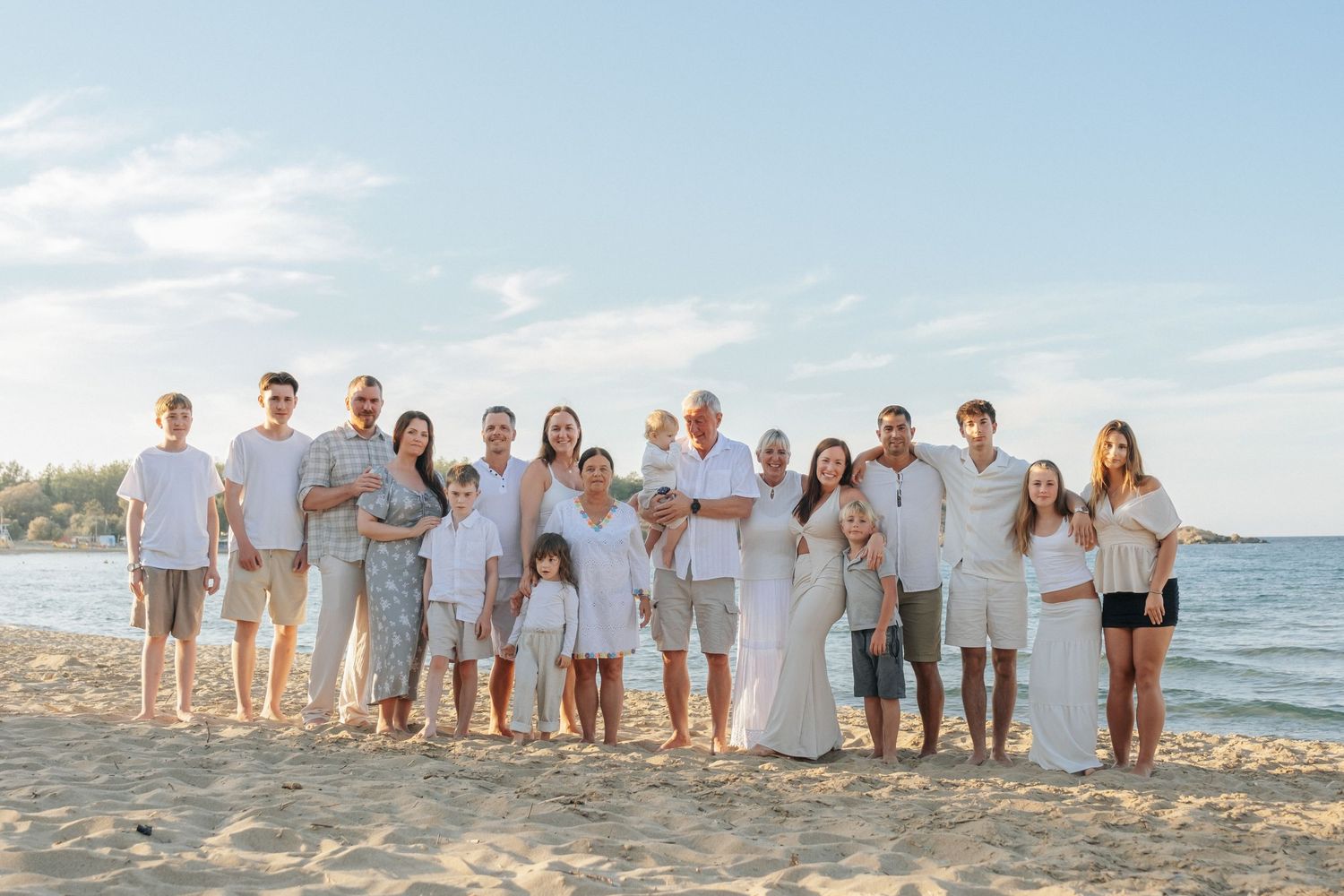 Large extended family group portrait on a sandy beach under a blue sky.