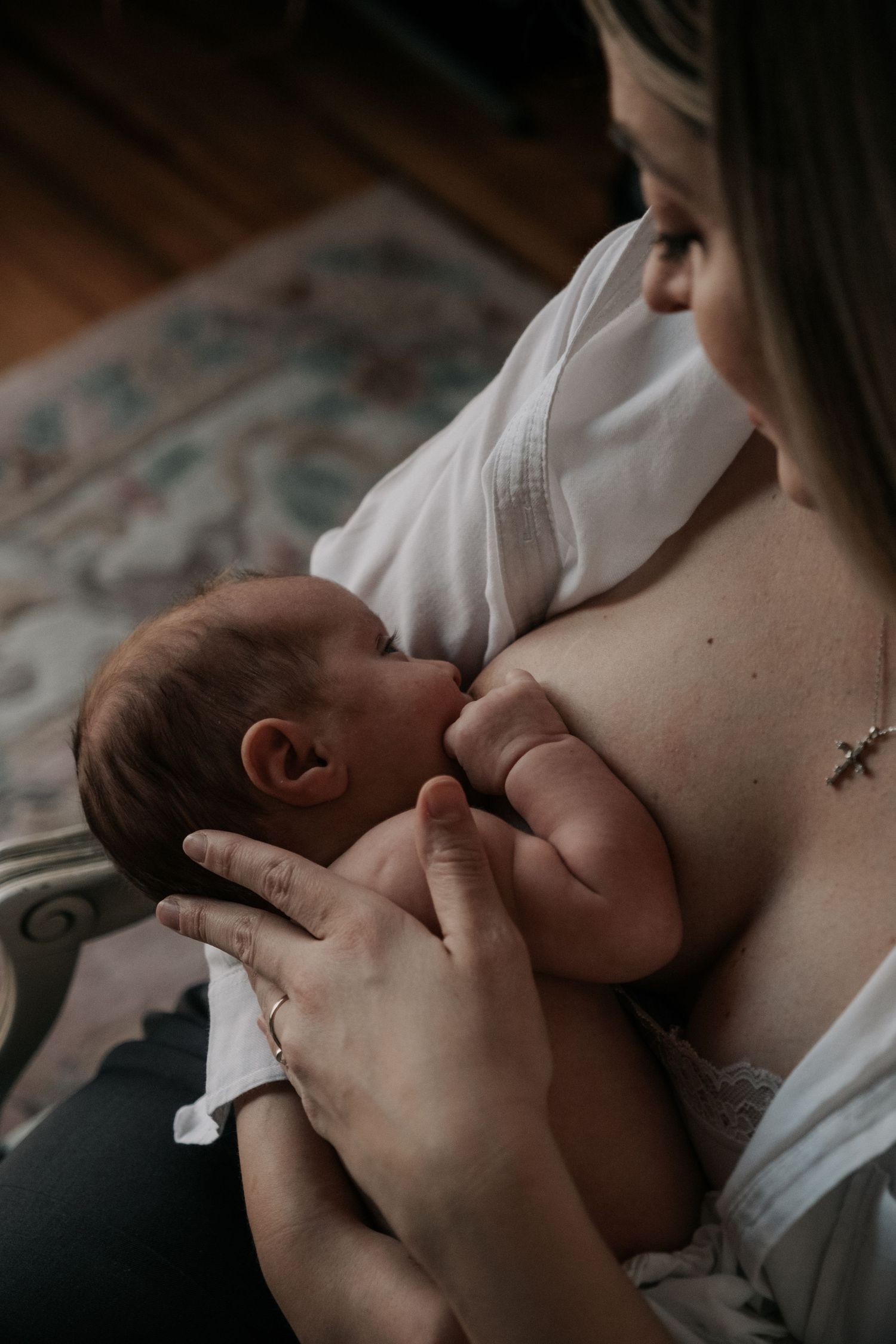Mother breastfeeding newborn baby in softly lit indoor setting with vintage chair.