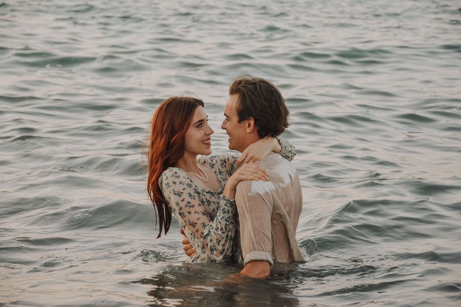 Happy couple embracing and smiling at each other while standing in ocean water.