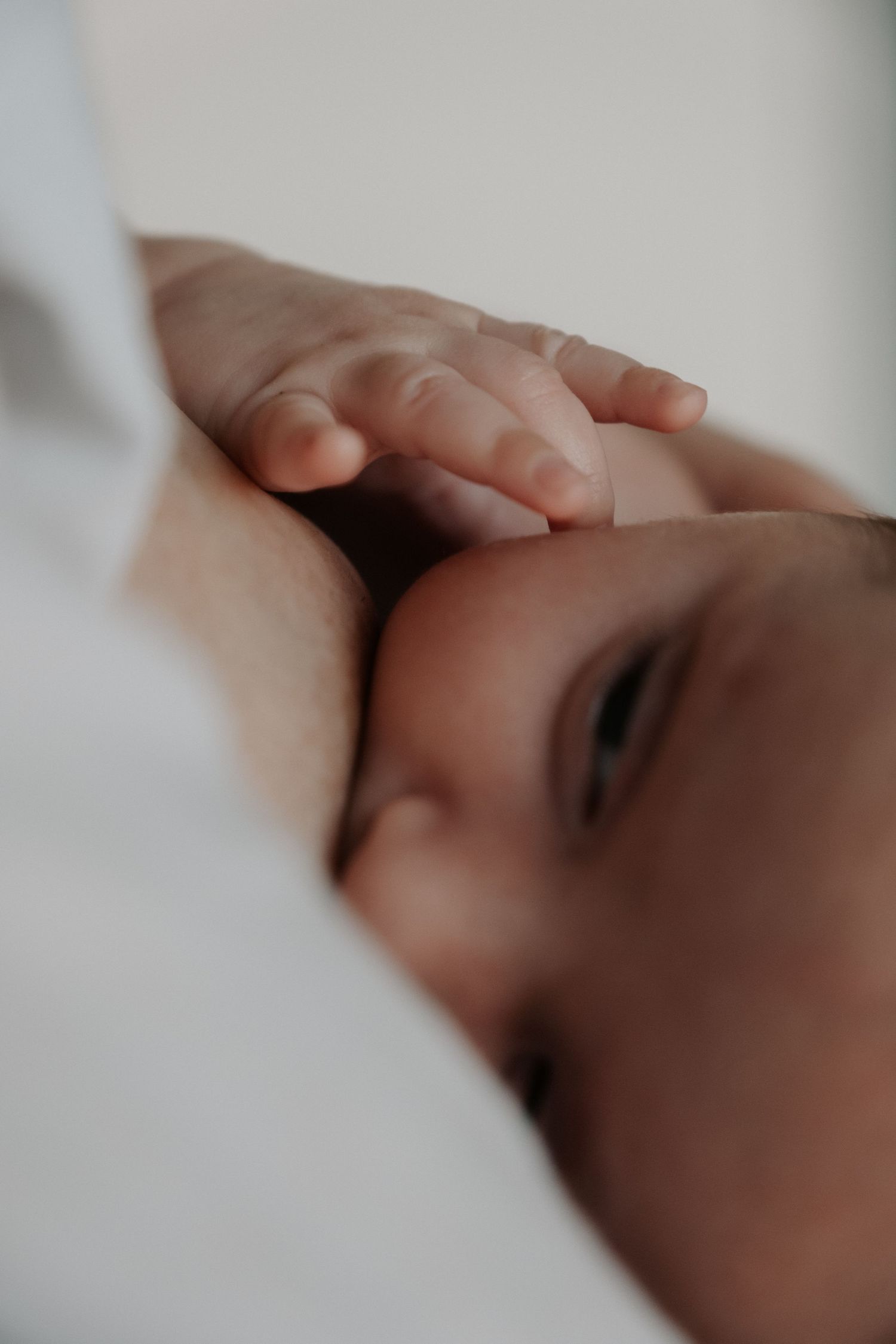 Close-up of sleeping newborn's face with tiny fingers curled near mouth on white background.