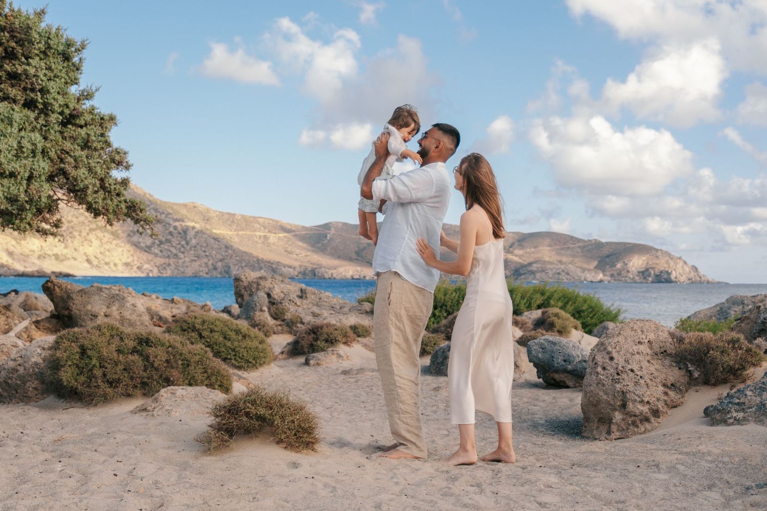 Happy family with a baby at a scenic rocky beach with blue sea and mountains.