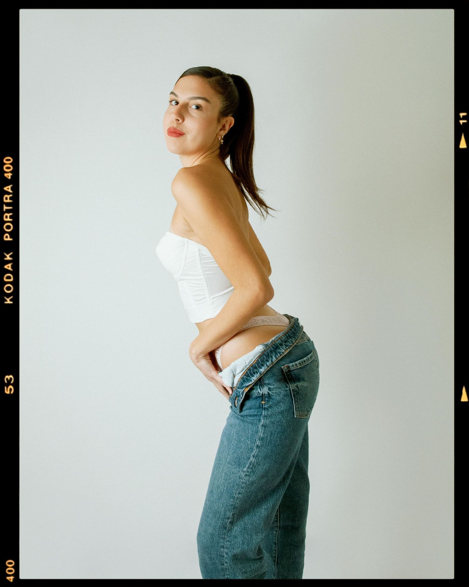 Young woman in white corset top and baggy jeans posing sideways on Kodak Portra film photo.