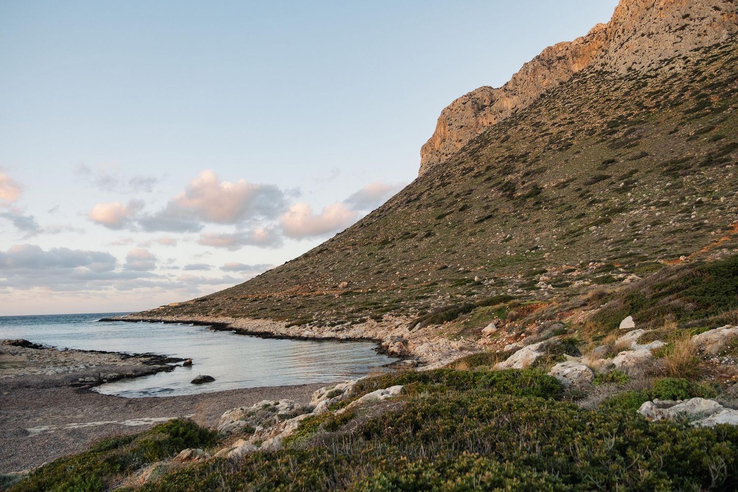 Rugged rocky hillside slopes down to a quiet secluded bay at dusk on Crete island.