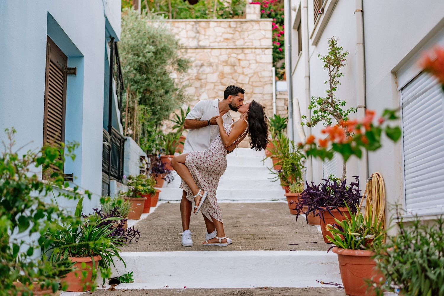 Couple sharing a romantic dip kiss on a charming Mediterranean alley lined with potted plants.