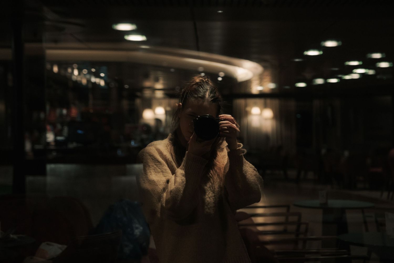 Photographer capturing mirror selfie with camera in dimly lit restaurant with warm ambient lighting.