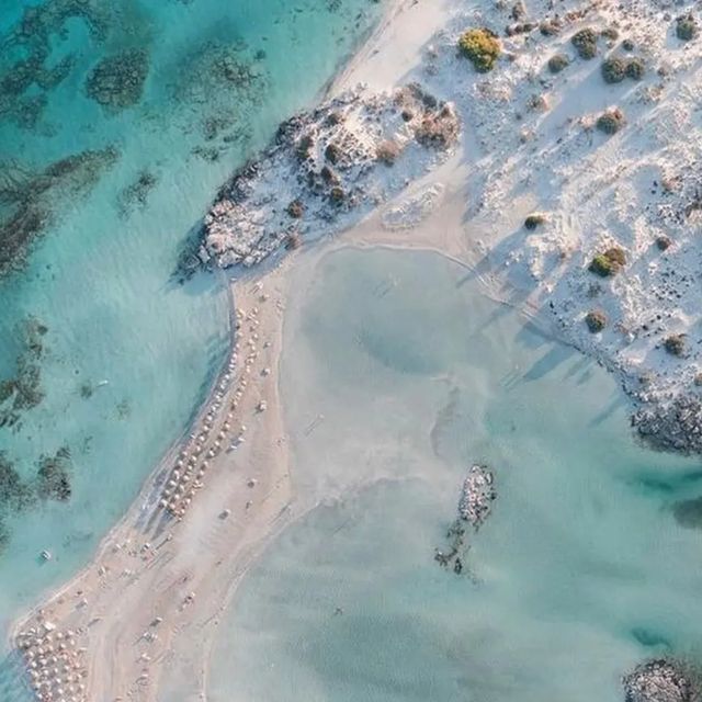 Aerial view of a stunning turquoise lagoon with white sand beach and scattered beach umbrellas.