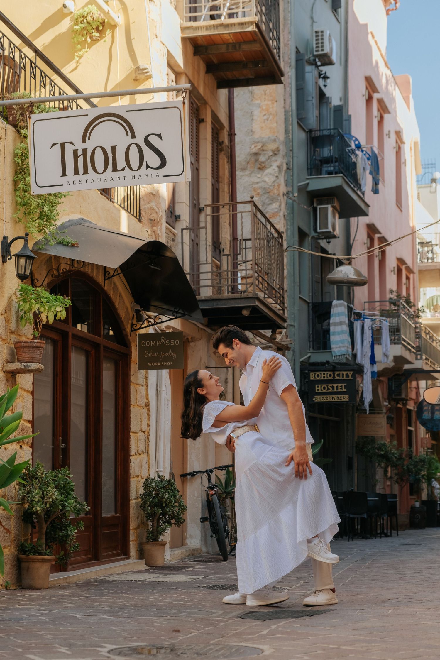 Couple dancing in a charming European alleyway, man dipping woman in white dress.