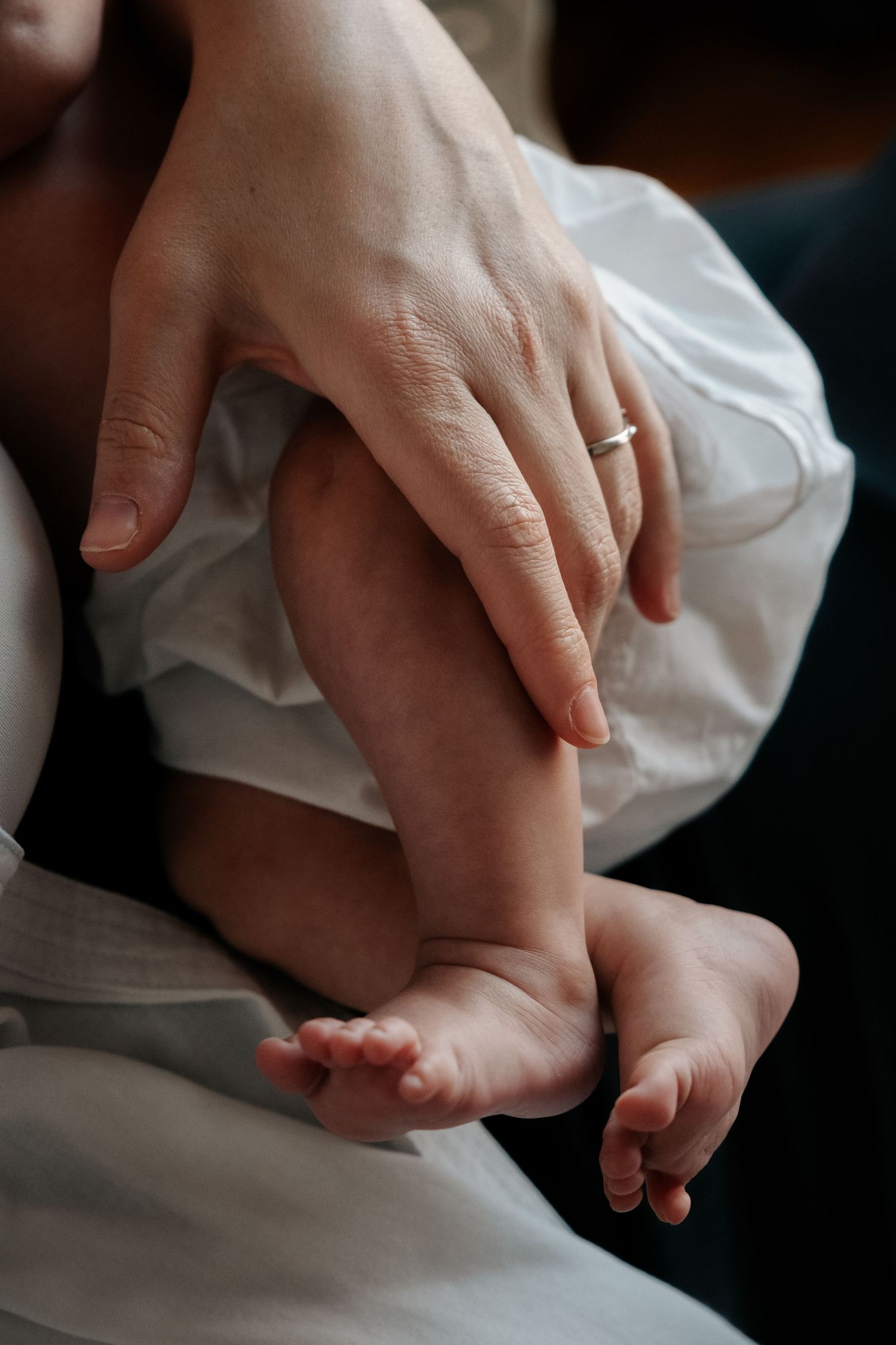 Close-up of a mother's hand with wedding ring gently holding her newborn baby's delicate feet.