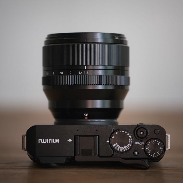 Top view of Fujifilm mirrorless camera with 56mm f1.2 lens on wooden surface.