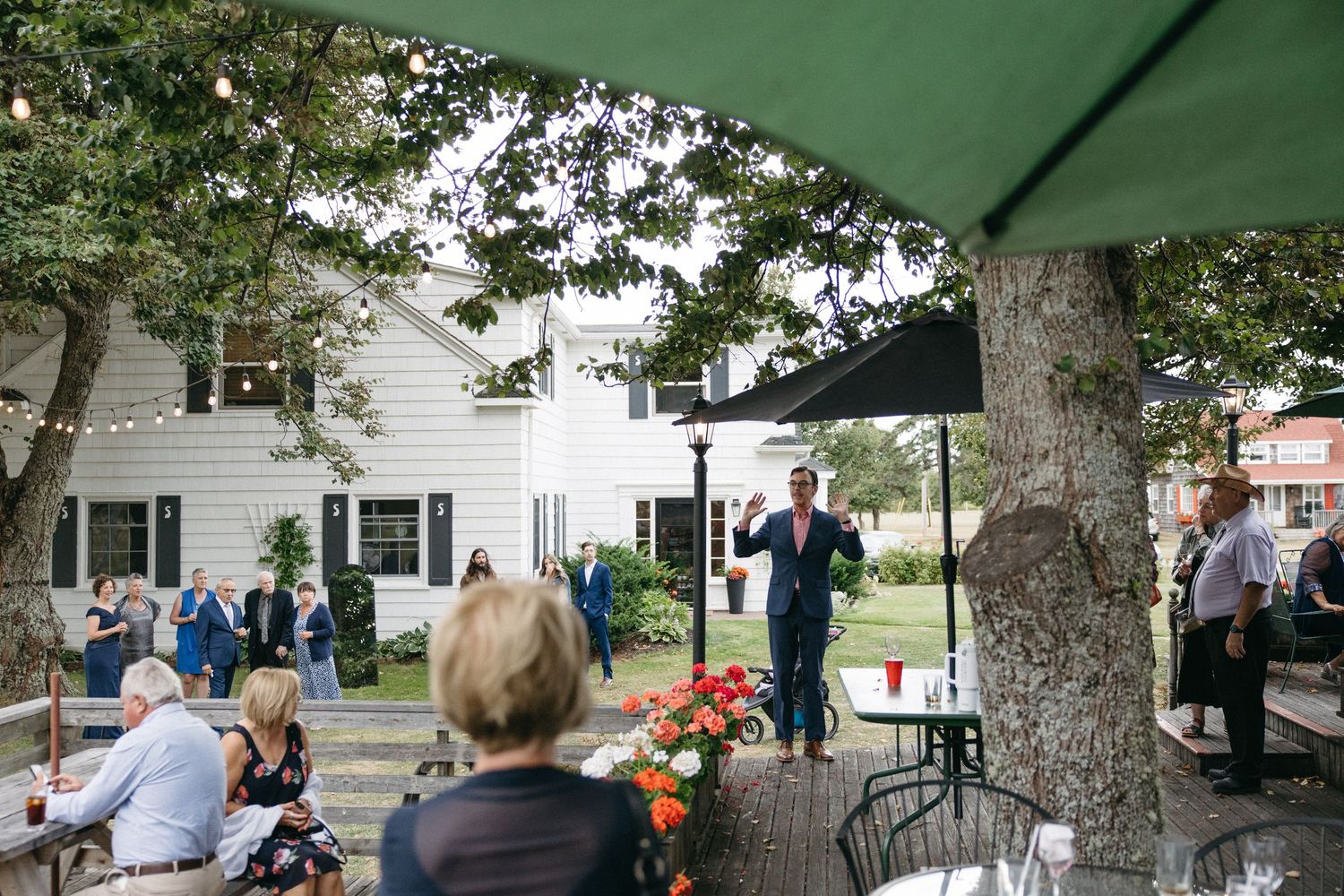 Wedding guests mingling outdoors under trees at a charming white venue during a reception cocktail hour.