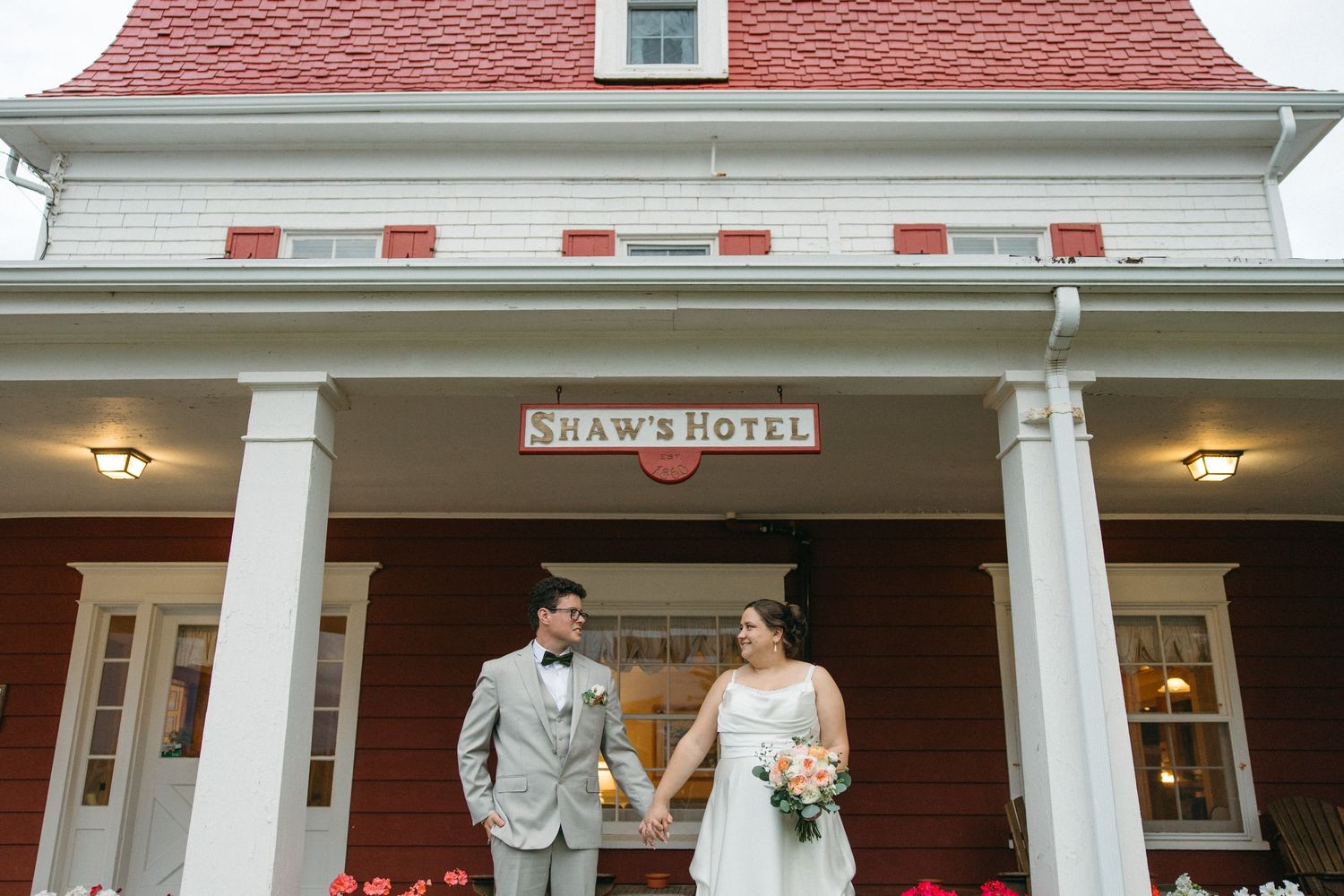 Bride and groom holding hands in front of Shaw's Hotel red and white historic building.