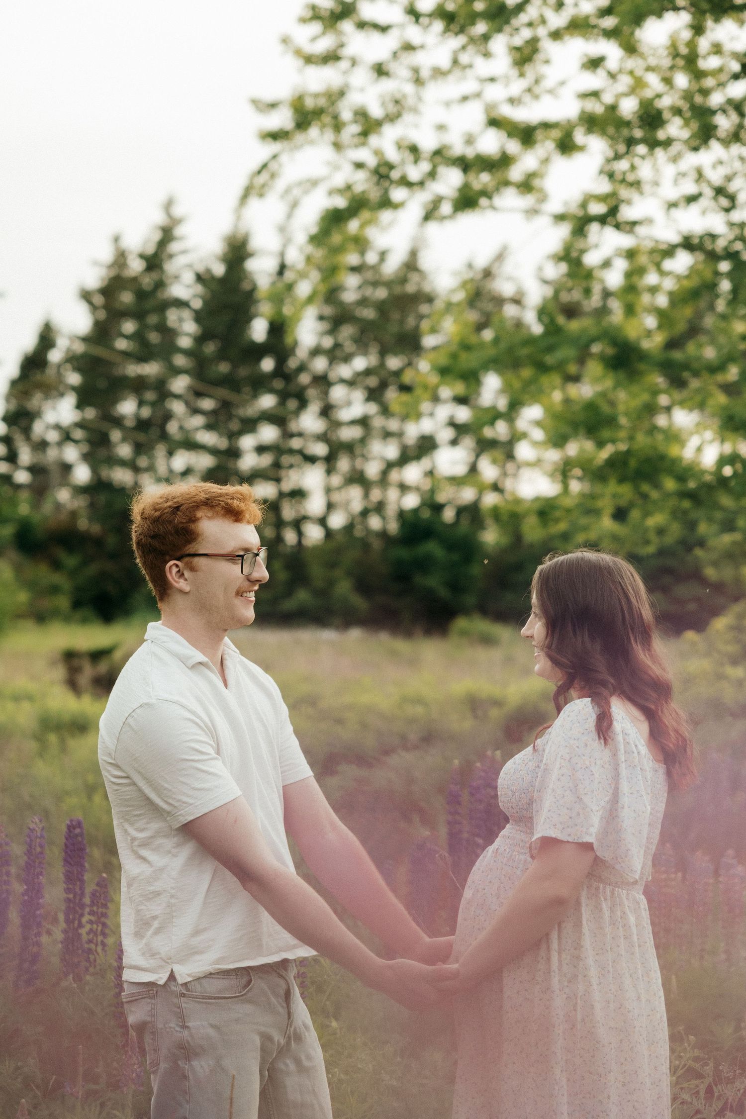 A couple walks through a field of purple lupines during a romantic summer photoshoot at sunset.