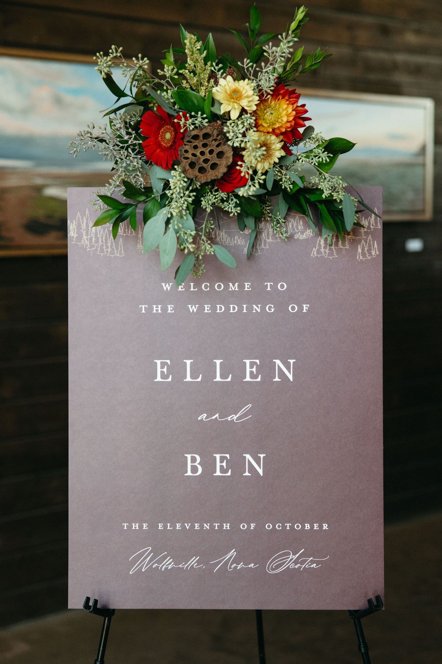 Wedding welcome sign with floral decorations displaying 'Ellen and Ben' in elegant typography.