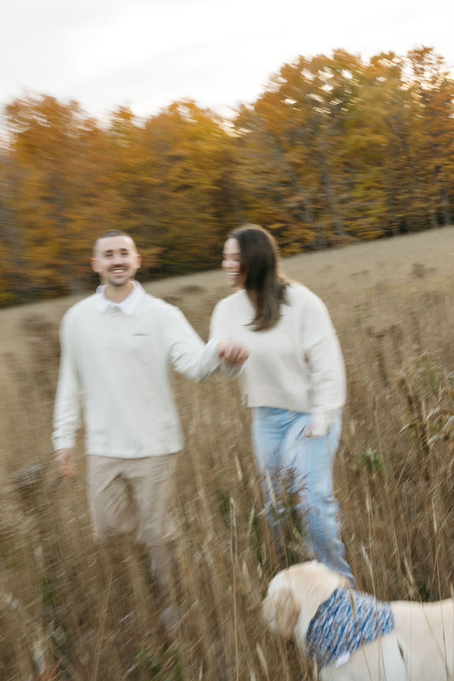 Candid autumn photoshoot with a couple and their dog in a grassy meadow.