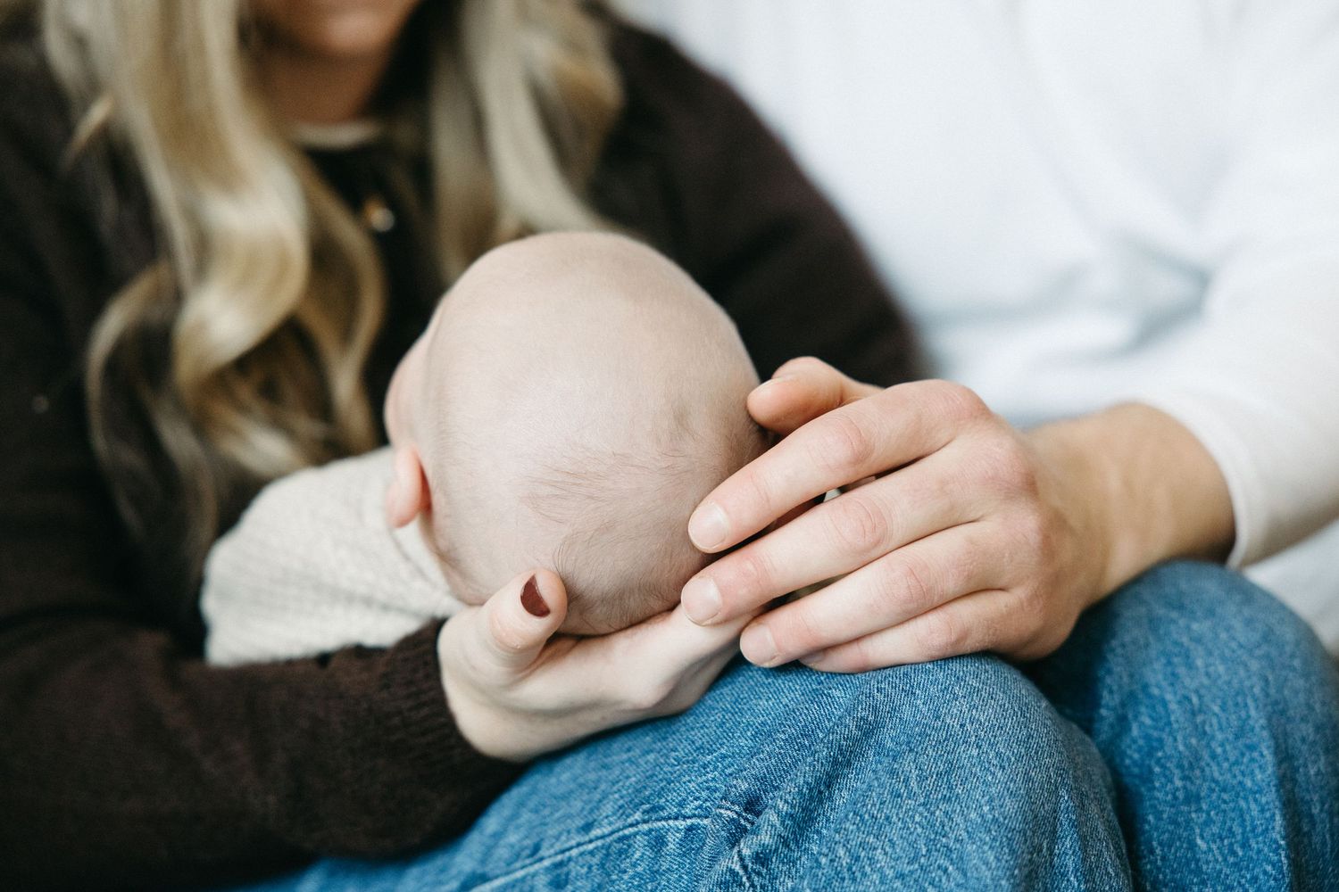 Close up of gentle hands holding baby on lap in denim jeans.