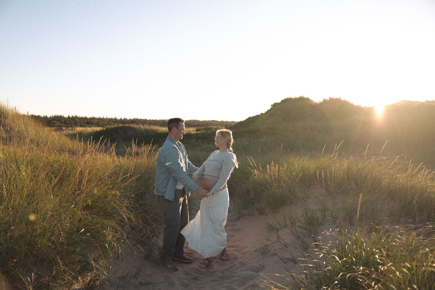 A romantic sunset moment captured between two people on a sandy path with tall grass.