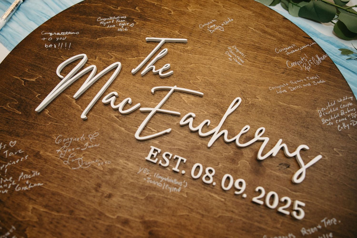 Wooden wedding guest book board with white handwritten signatures and messages.