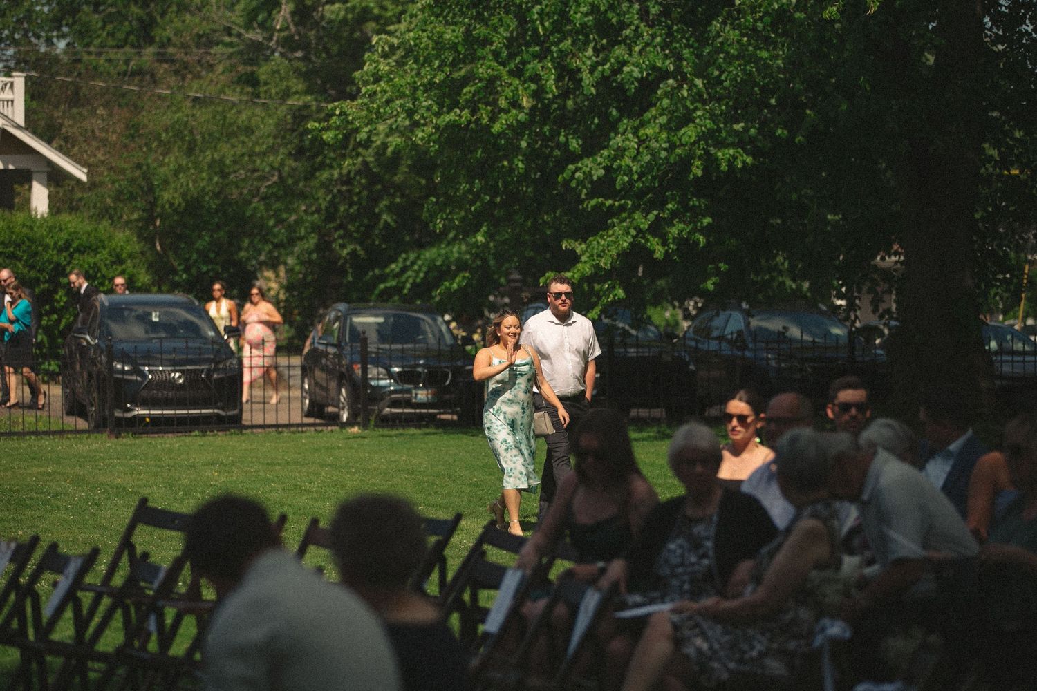 Wedding guests gather outdoors on lawn during summer celebration.