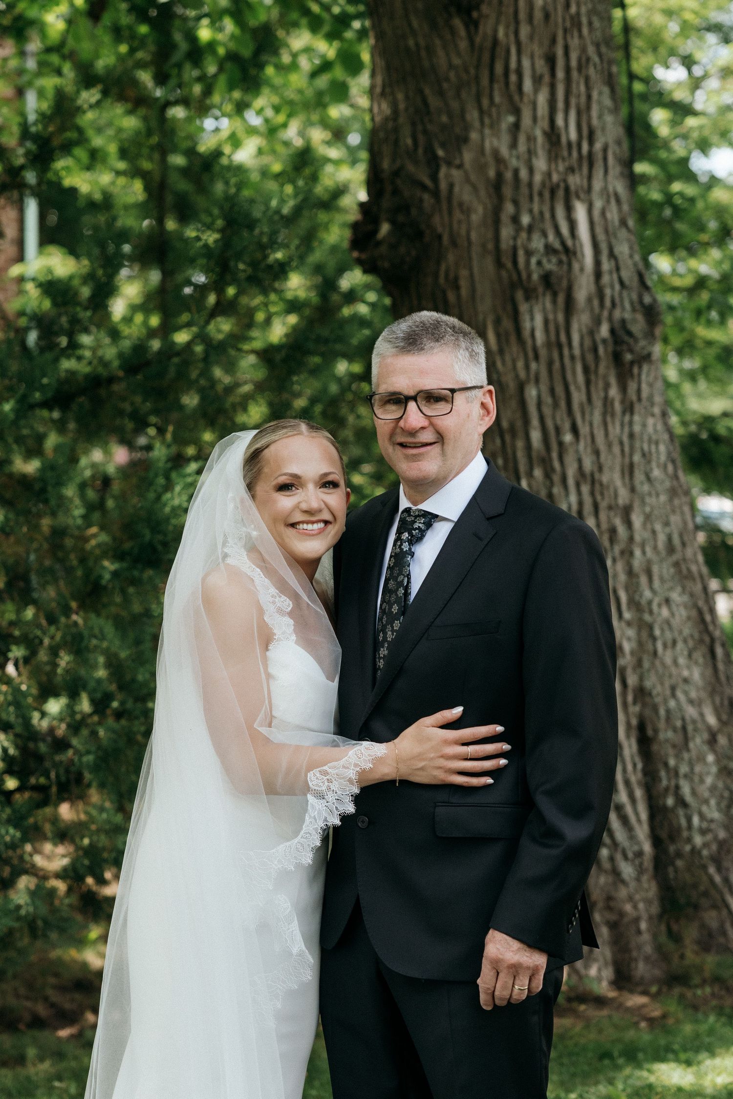 Wedding portrait taken outdoors against large tree trunks in natural lighting.