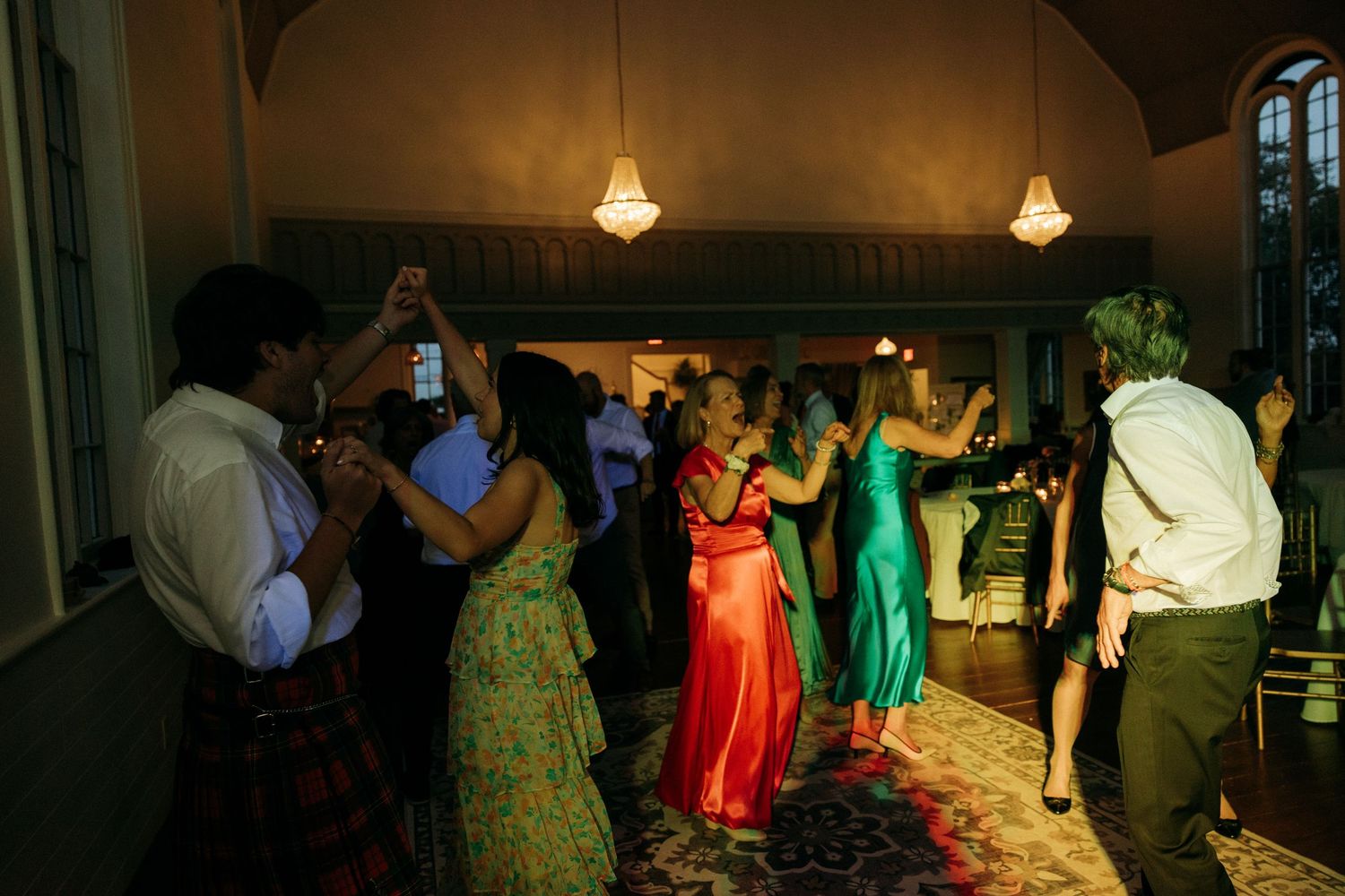 Wedding reception guests dancing under warm lighting in colorful attire.
