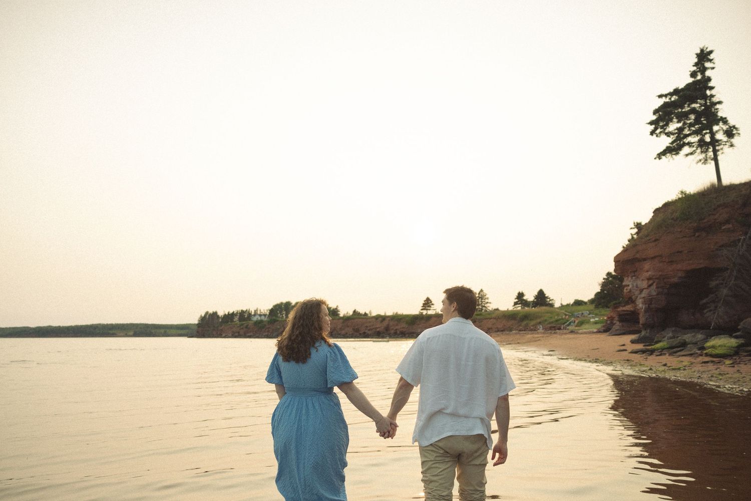 A couple walks hand in hand along a scenic beach during sunset.