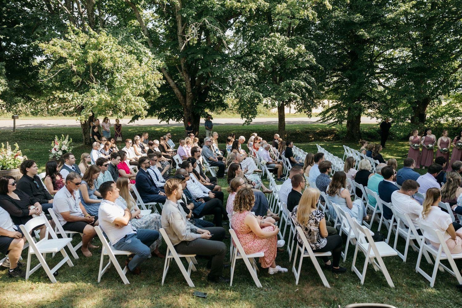 Wedding guests seated in rows of white chairs during an outdoor ceremony.