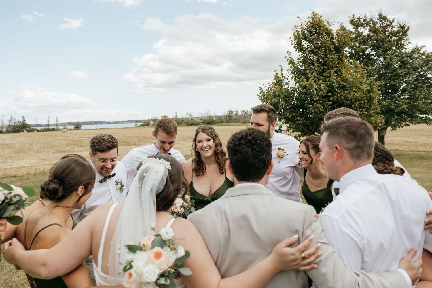 Wedding party celebrating together in a joyful group hug outdoors near a scenic waterfront venue.