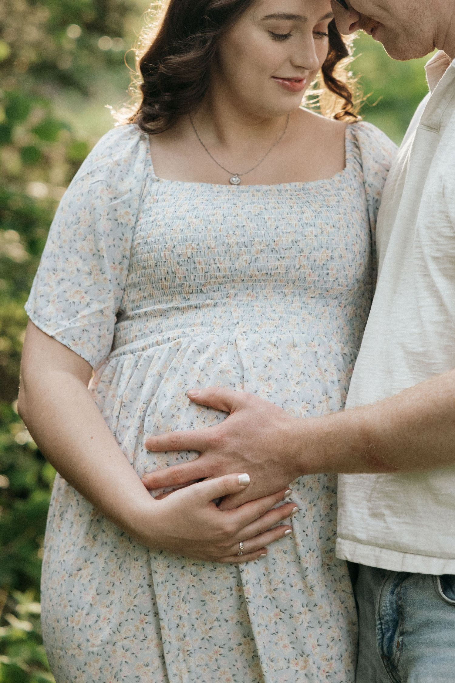 Gentle maternity photos showing loving hands cradling a baby bump in a floral dress.